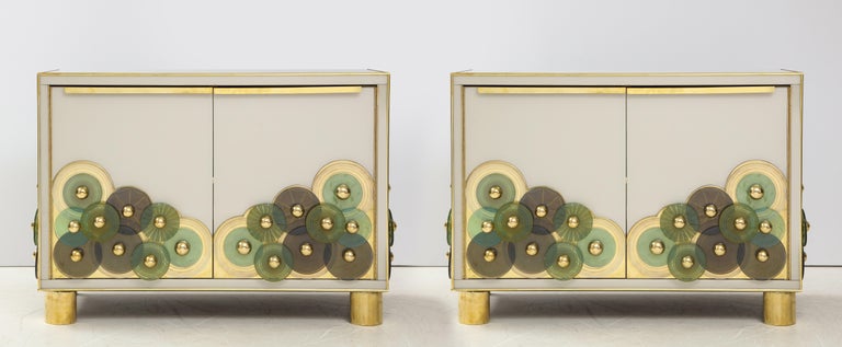 One of a kind pair of sideboards designed by Karina Gentinetta and handmade in Venice, Italy by a master artisan and artist. Wooden frame is veneered in Ivory hand-tinted Murano glass panels with brass inlays. Hand-casted Murano glass discs, both