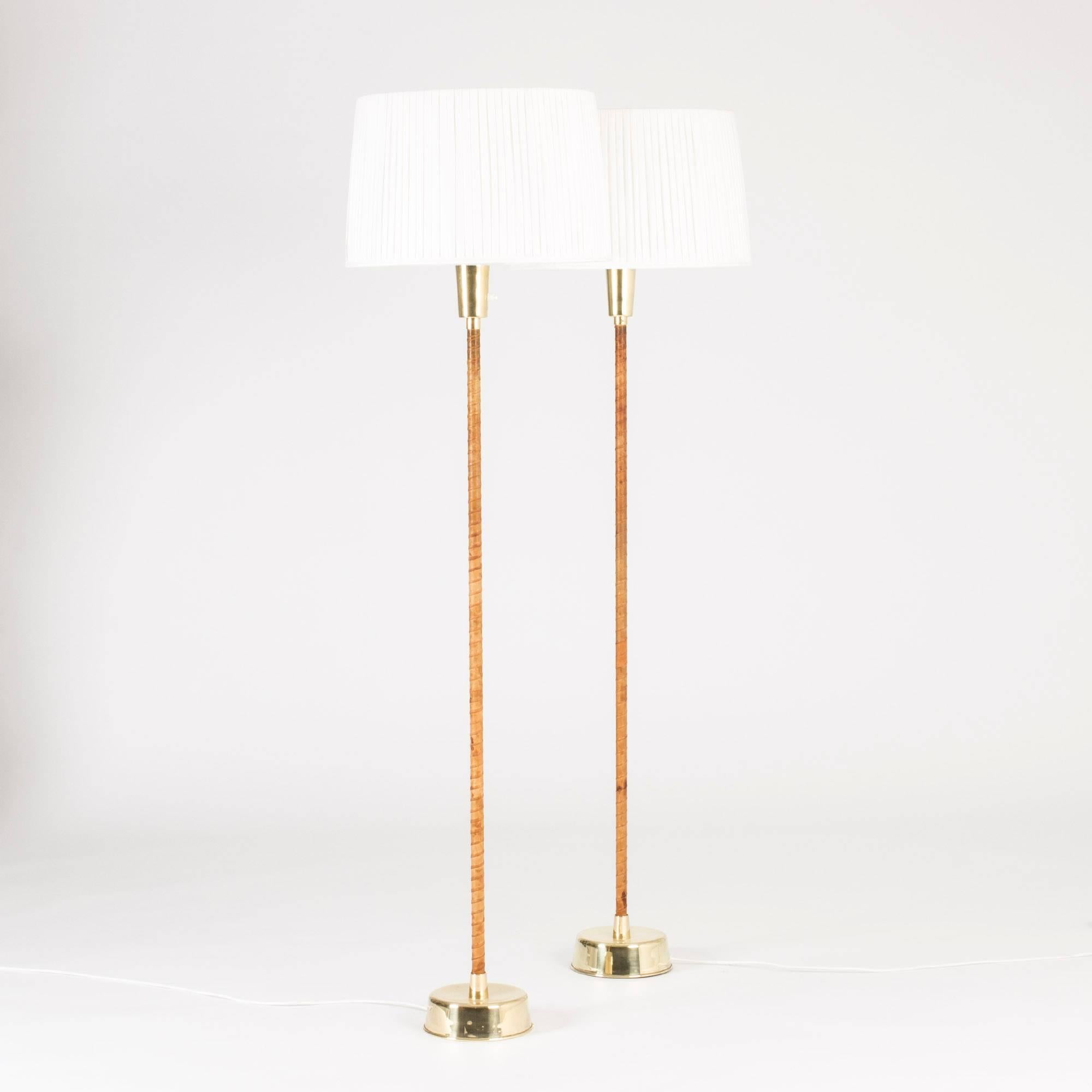 Pair of floor lamps by Lisa Johansson-Pape, striking in their poised simplicity. Brass bases and brown leather wound handles, voluminous white lamp shades.