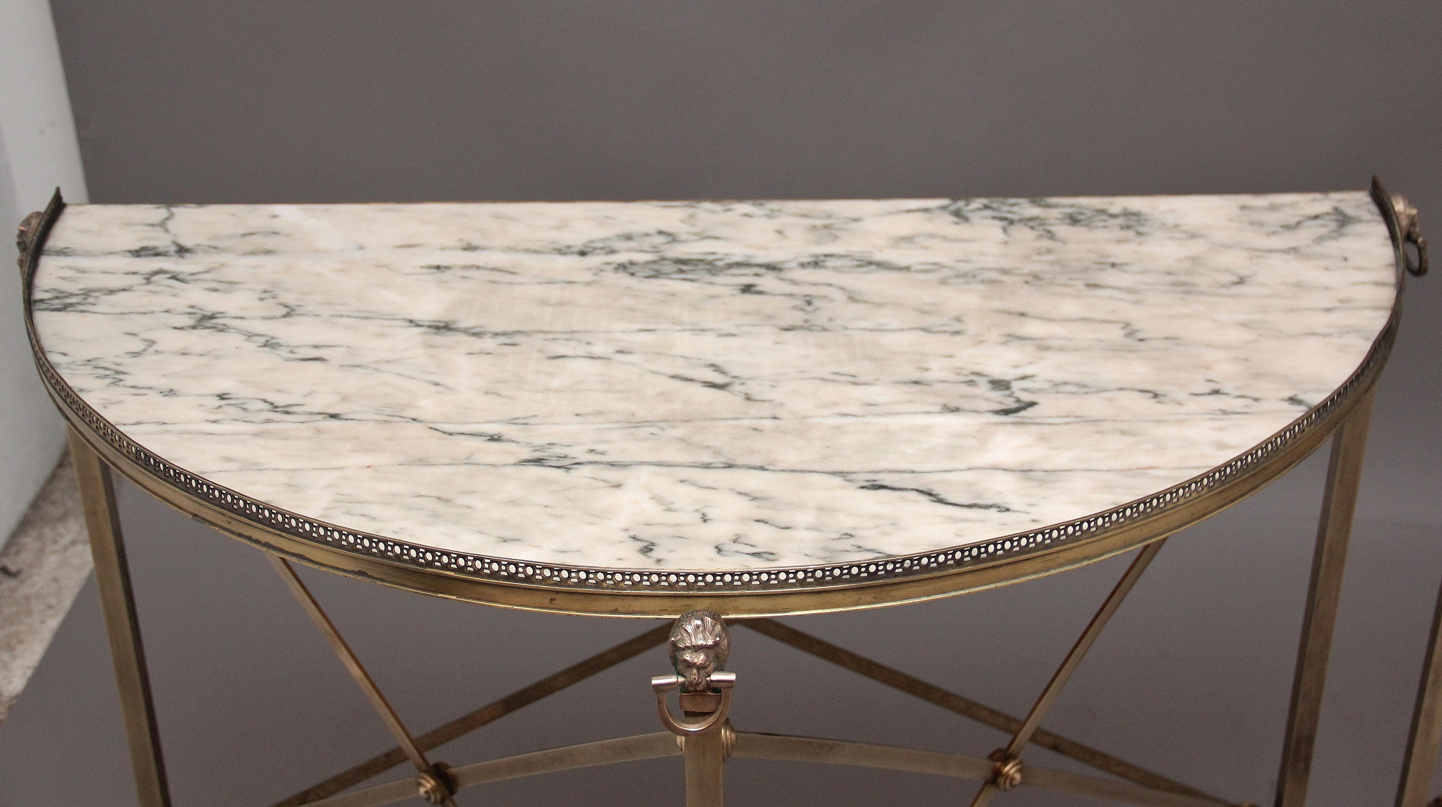 A decorative pair of mid 20th Century French brass and marble top demi lune console tables, having the original veined marble top with a decorative pierced frieze running along the outer edge, supported on three brass legs terminating on claw feet,