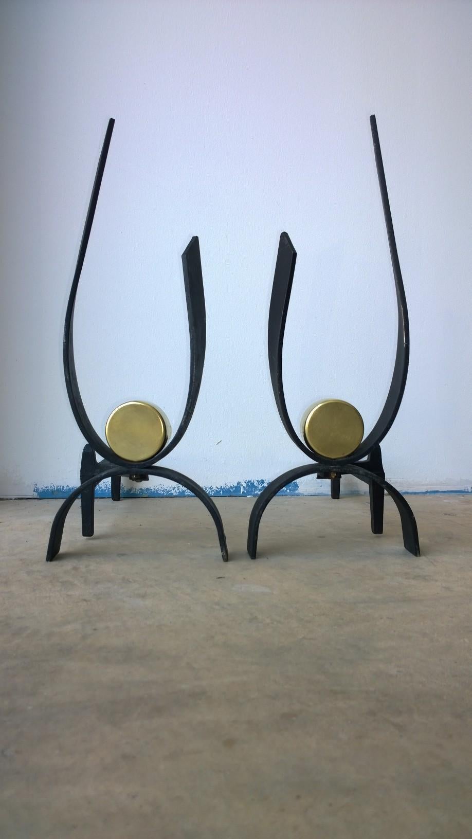 Offered is a pair of metal and brass Mid-Century Modern fireplace andirons by Donald Deskey. The pair are an elegant design with clean modern lines with just a touch of shiny brass. Even without a 