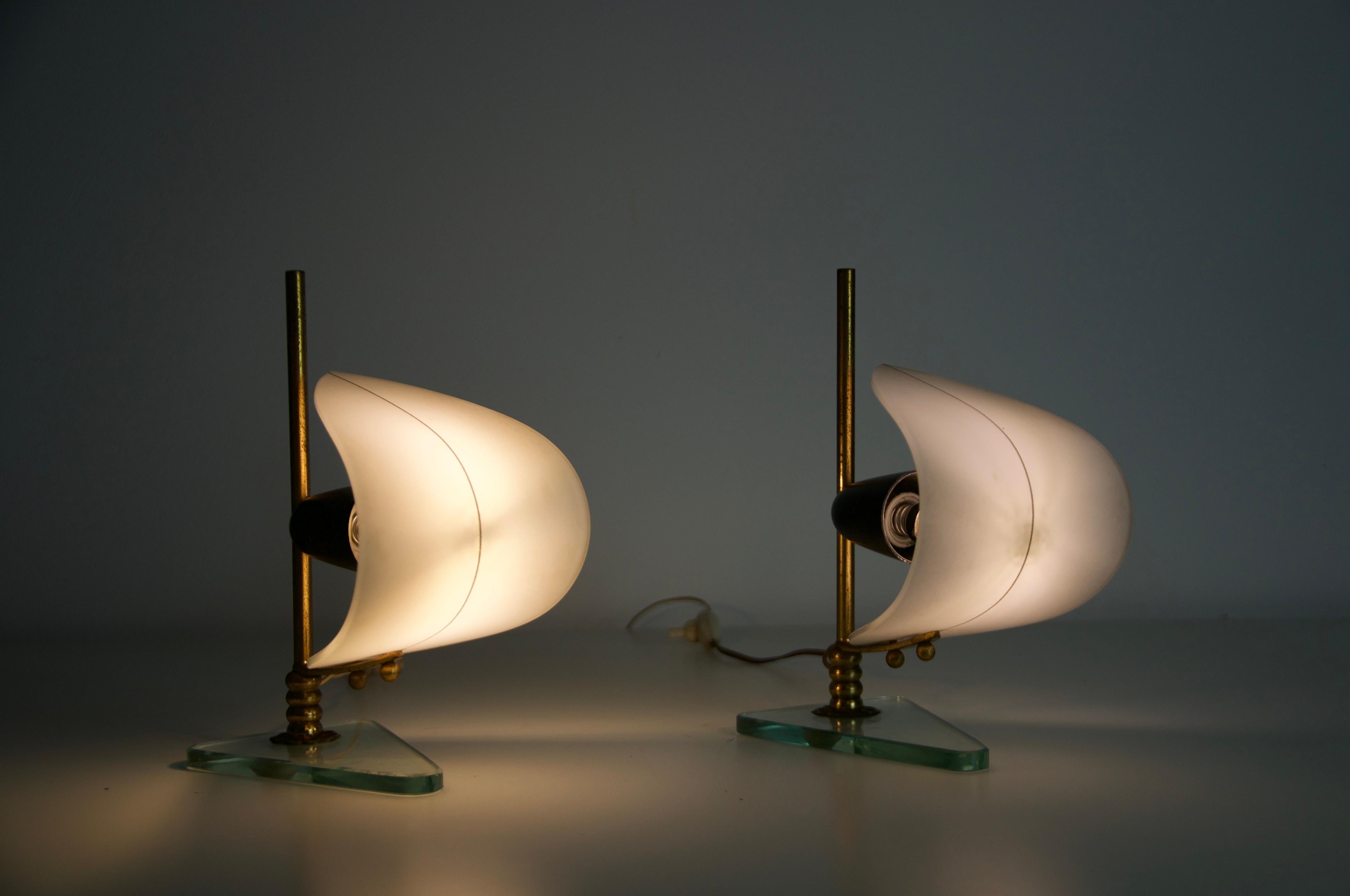 This exceptional pair of Italian table lamps from the 1950s captivates with their sculptural, sailboat-inspired design. Each lamp features a slender brass rod mast, resting on a clear glass base shaped like a boat hull. The opaline glass shades