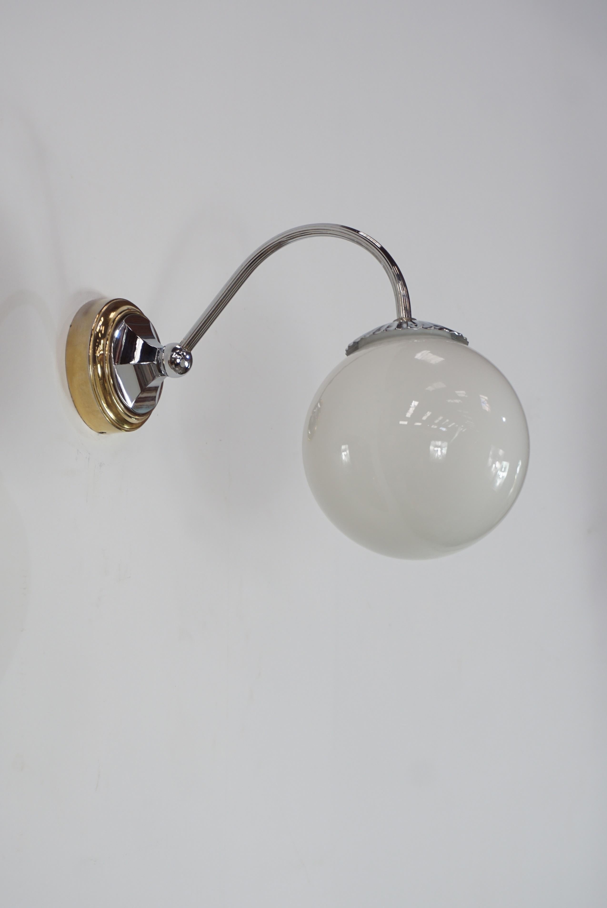 Bright and sparkling pair of wall sconces with white opaline ball shaped on a brass structure.