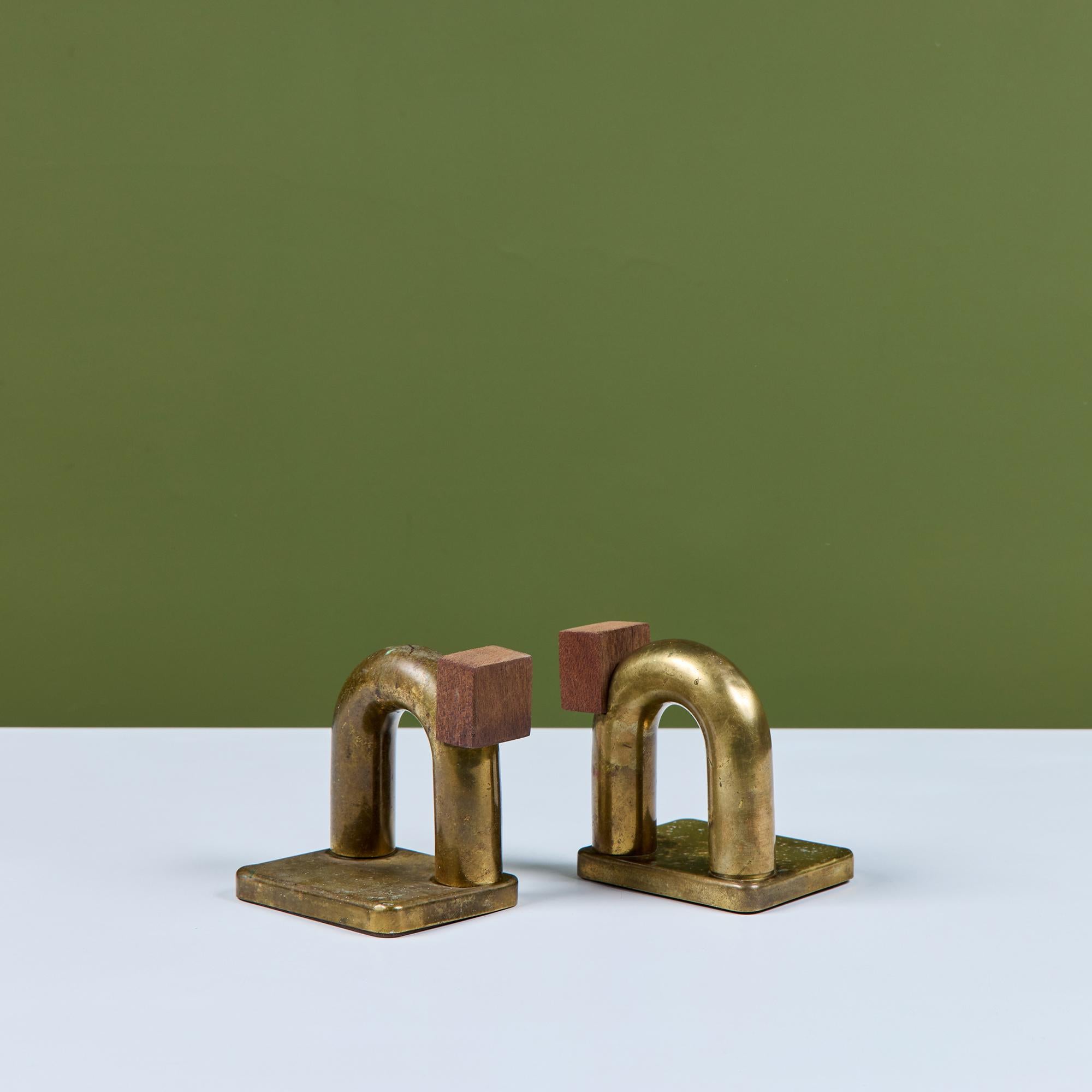 Pair of brass and wood bookends by Walter von Nessen for Chase, c.1930s, USA. The pair of bookends feature two brass figures with curved tubular bodies and geometric shaped wood heads. They rest upon a rectangular brass base.

 The Chase Brass and