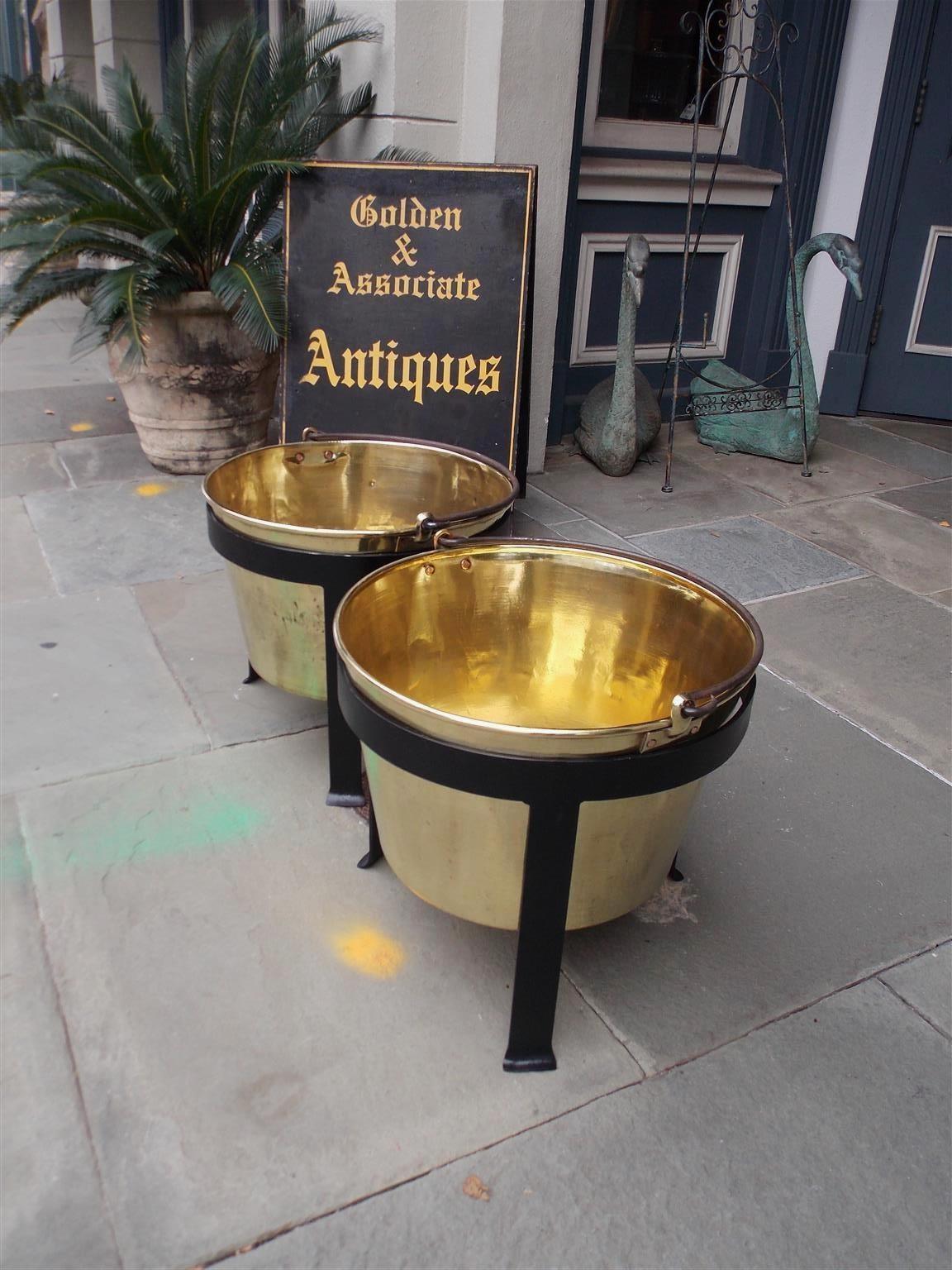 Pair of American brass and wrought iron plantation cauldrons with original scrolled handles fitted on a circular three legged banded stand with splayed feet. Mid-19th century stamped by maker Hiram W. Hayden, Waterbury, CT.