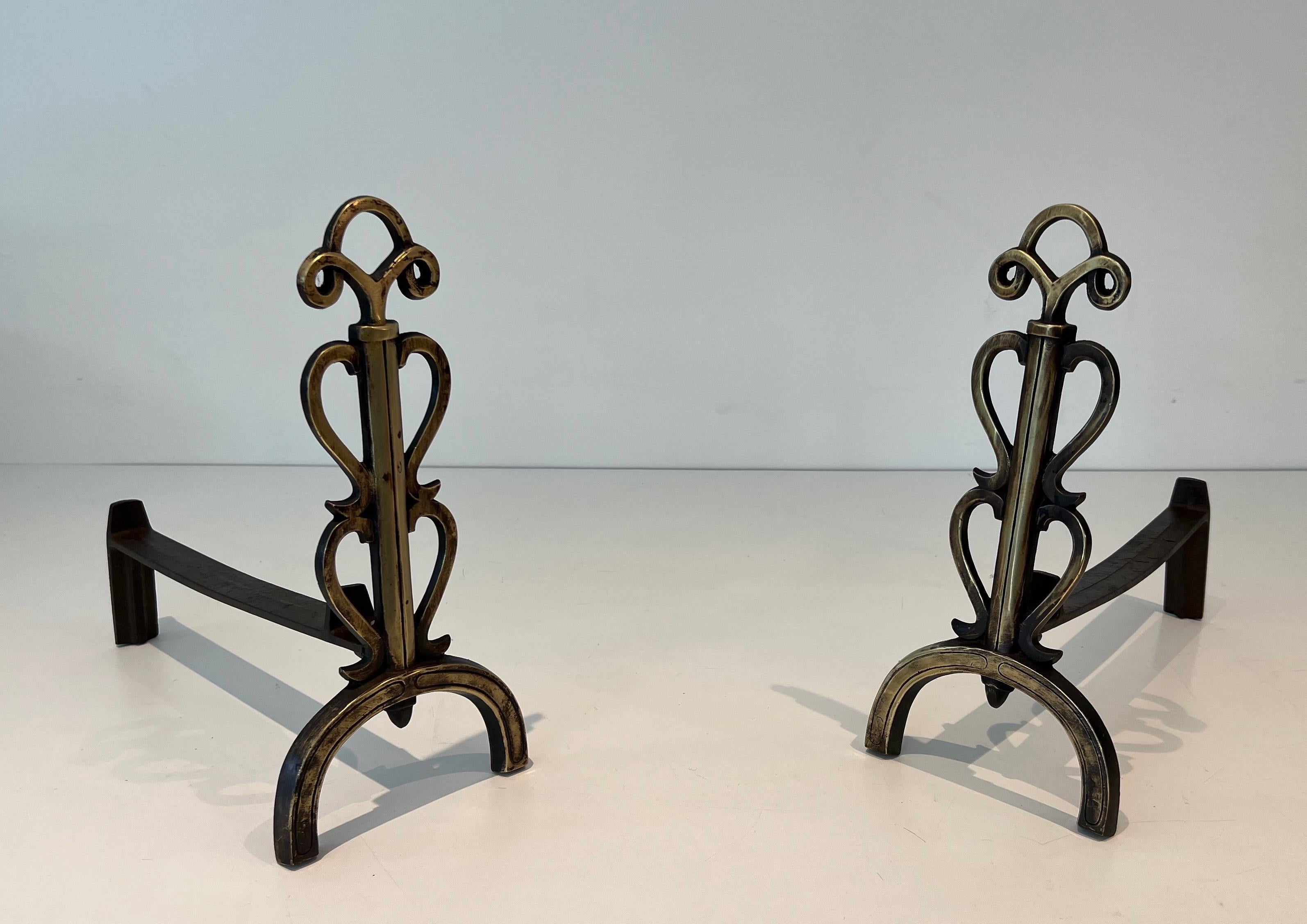 This elegant pair of design andirosn is made of brass and wrought iron. This is a French work in the style of Raymond Subes. Circa 1940