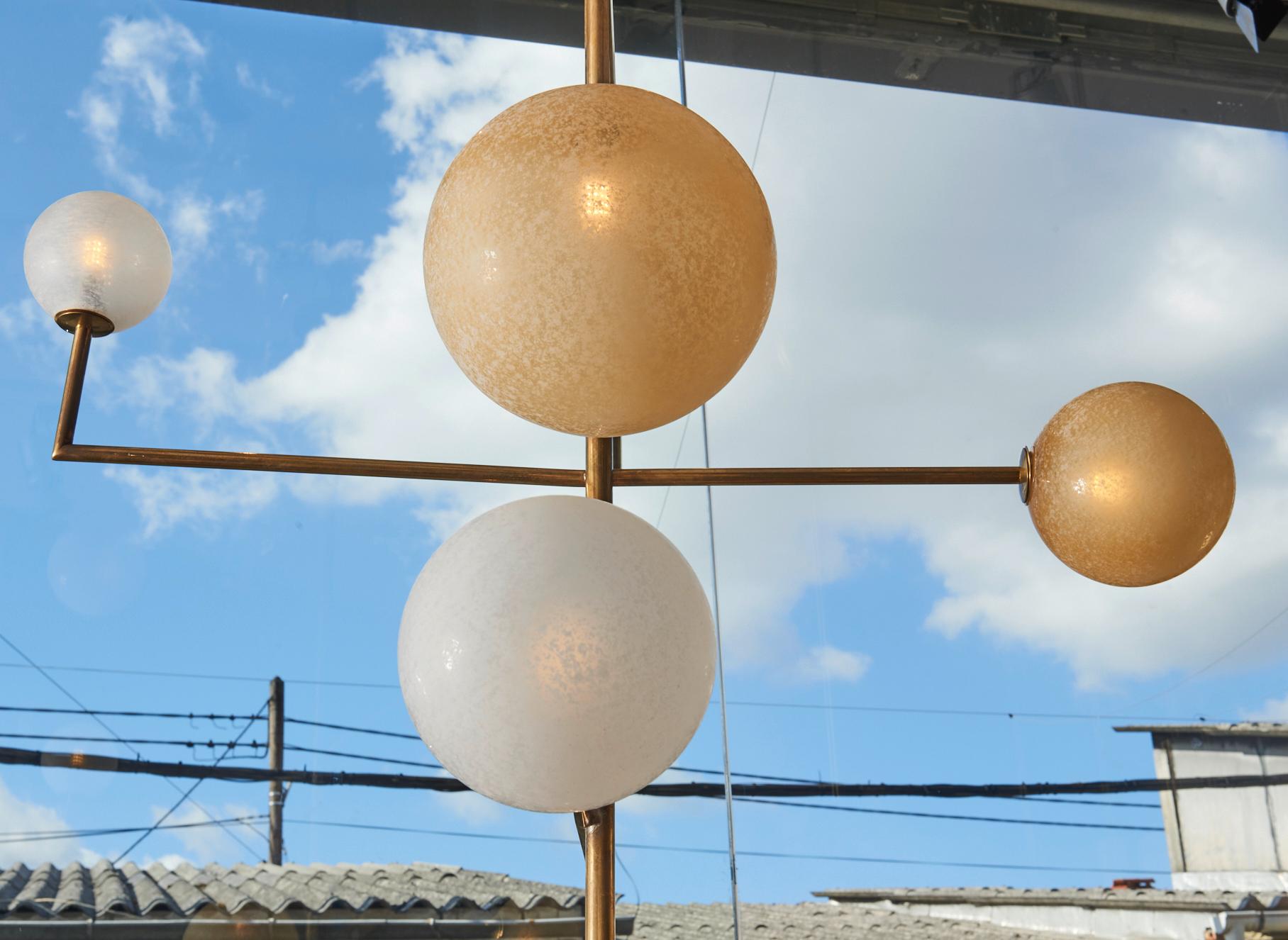 Pair of chandeliers made of a brass geometrical structure and frosted white and yellow globes.