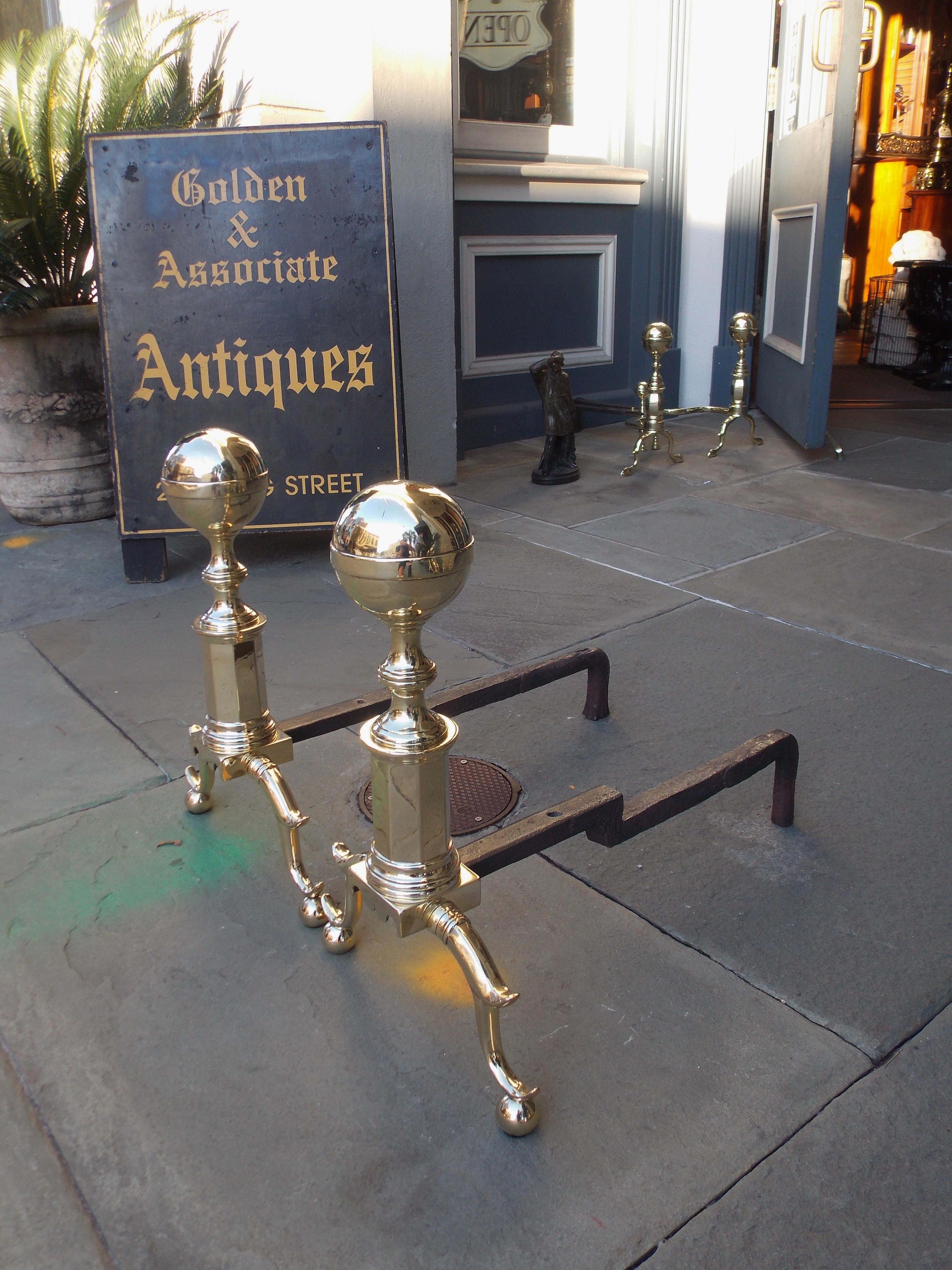 Pair of brass banded flanking ball finial andirons with faceted ringed plinths, scalloped skirts, original rear wrought iron dog legs, double spur banded legs, and resting on ball feet. Boston, Ma. Early 19th century.