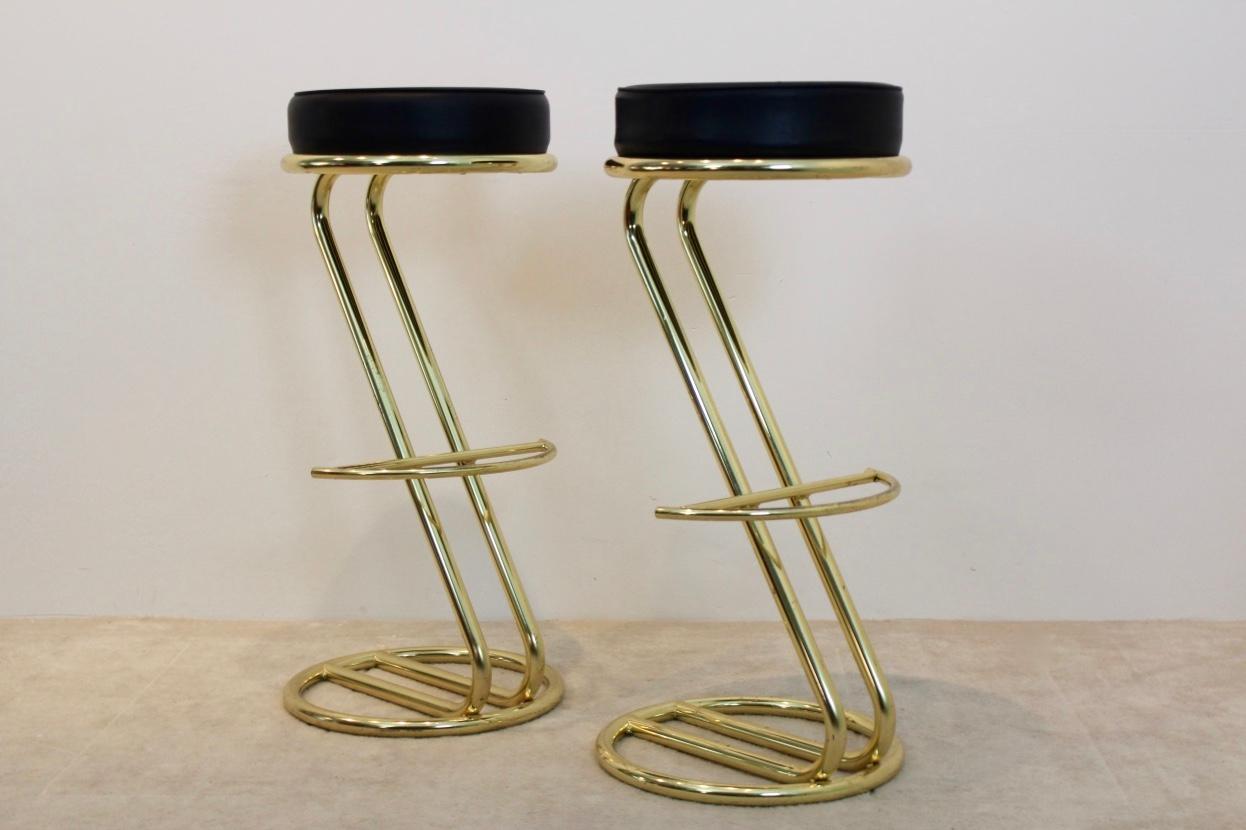 Symmetric pair of gold-plated bar stools with a glossy frame and a comfortable matching black leather seat. Newly upholstered with very nice leather. Features a nice comfy seat rest and a minimalist frame. Very good condition.