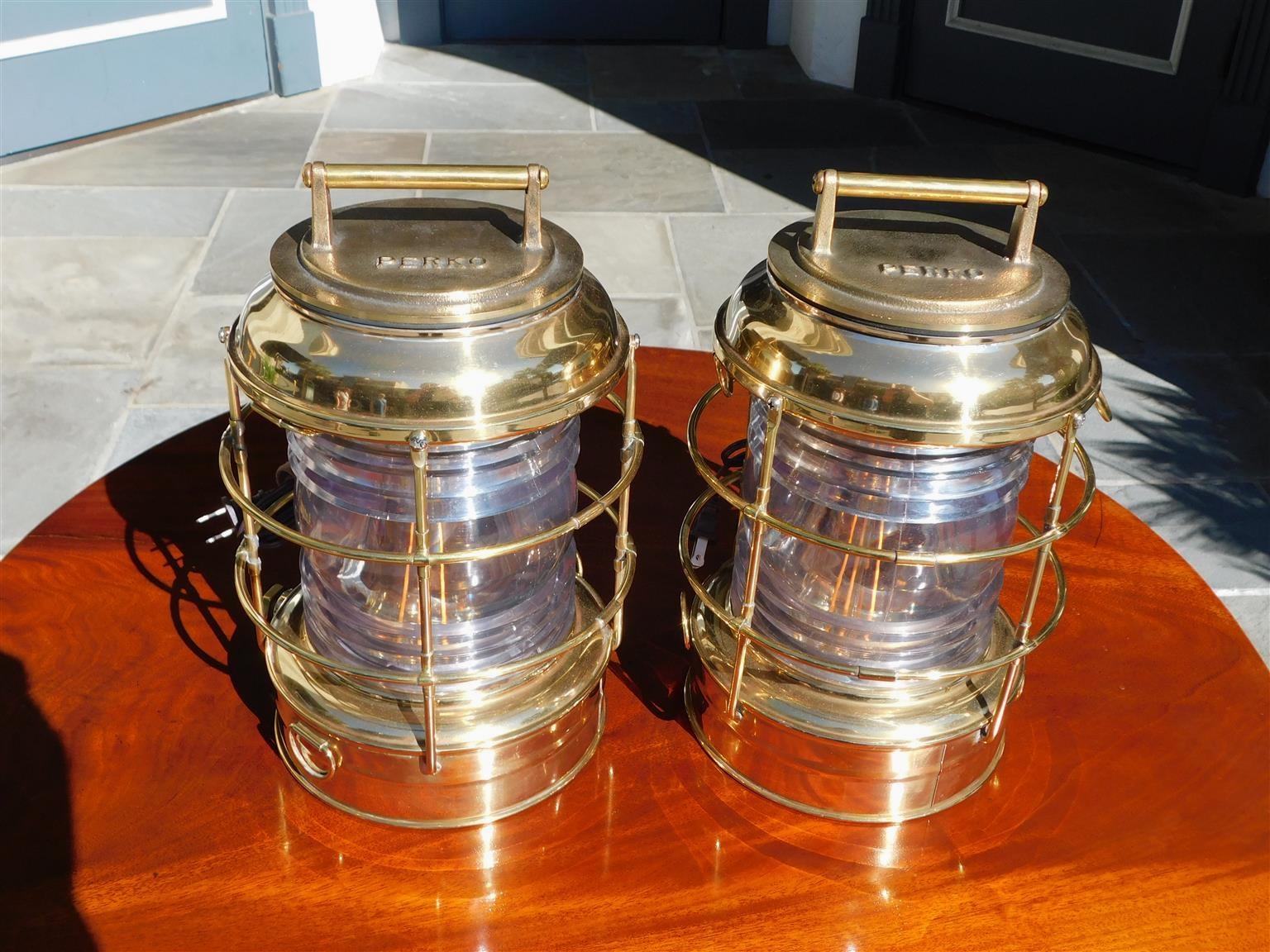 Pair of Brass Beacon Marine Lanterns with flanking threaded handle lids, protective exterior cages, and original clear Fresnel lenses. Pair of lanterns have been electrified. Stamped Perko Company, NY. Late 19th century.