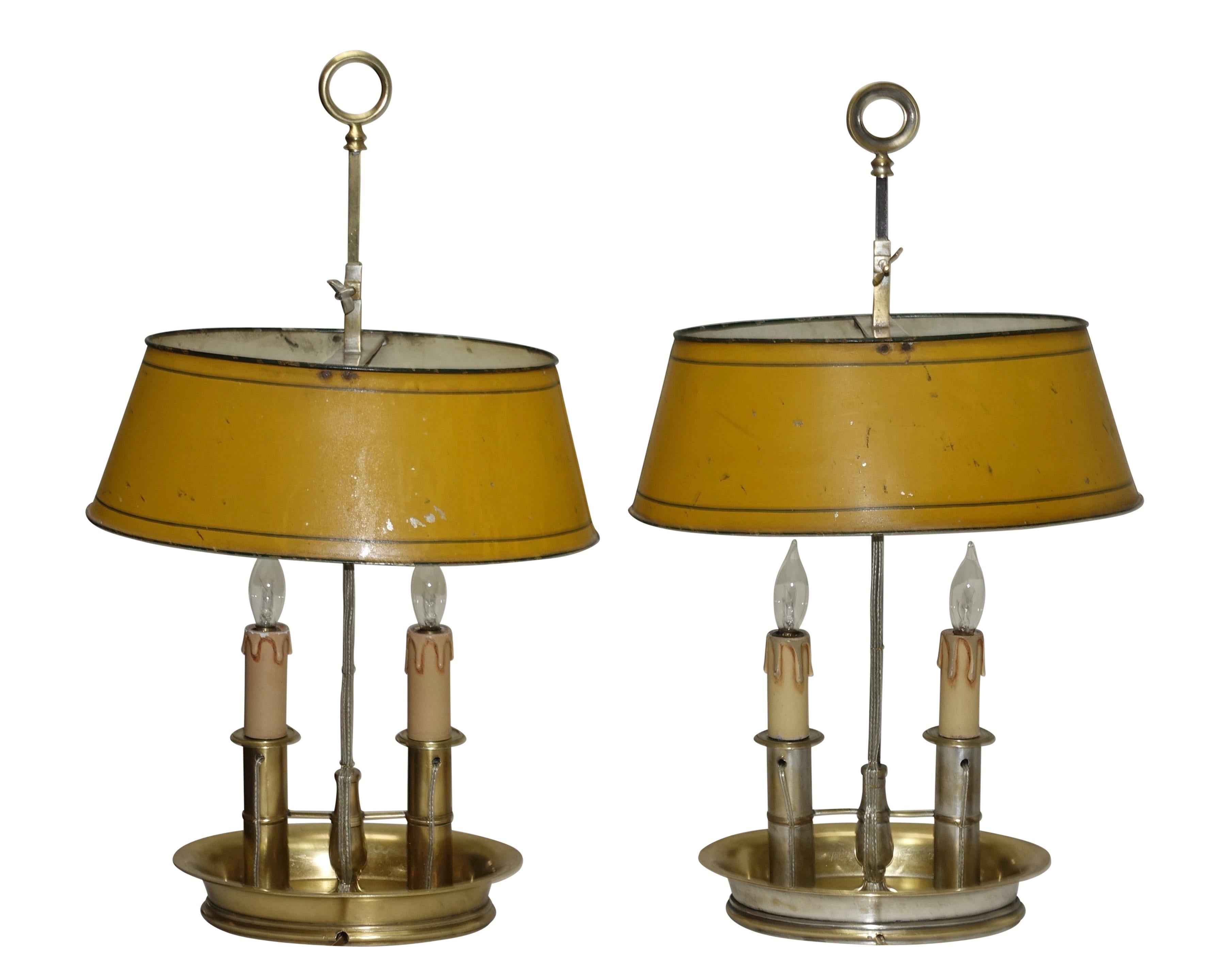 A charming pair of brass bouilotte lamps with mustard yellow tole' shades with a green pinstripe around the top and bottom of the shade. One of the lamps has remnants of silver plating. Two sockets up in the shade and two sockets in the