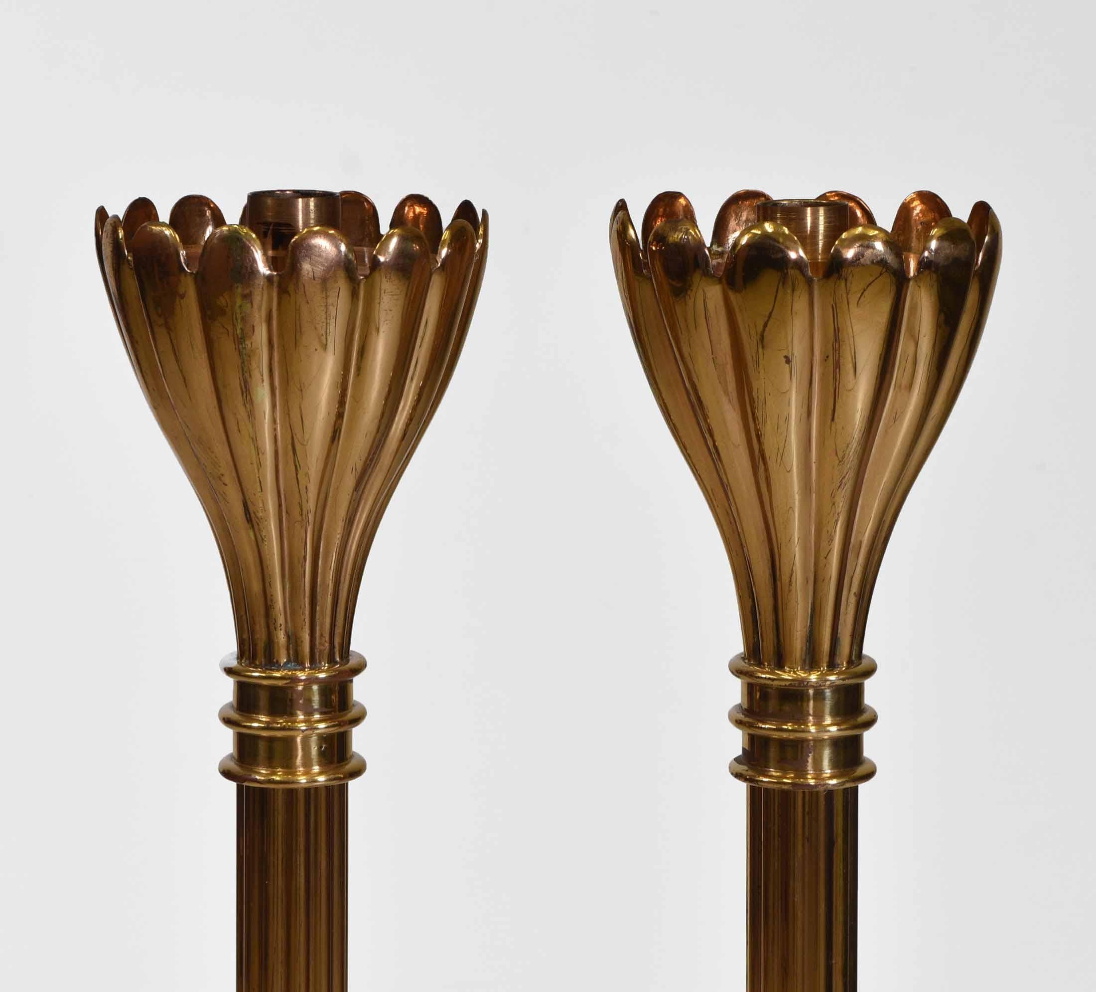 A pair of brass fluted floor standing candle stands with flared scalloped uppers and copper inset tops. Circa early to mid 20th century.

They have weighted bases, each one weighing 6kg. The candle diameter is 3cm. Two pairs available. 

There