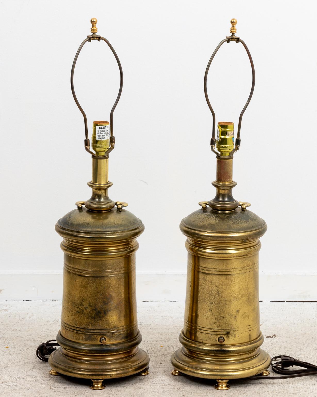 Circa 1950s robust pair of brass cylinder lamps on four brass feet with ring turned detail. Made in the United States. Please note of wear consistent with age including pitting and wear to the brass. The piece measures 28.00 Inches height to finial.