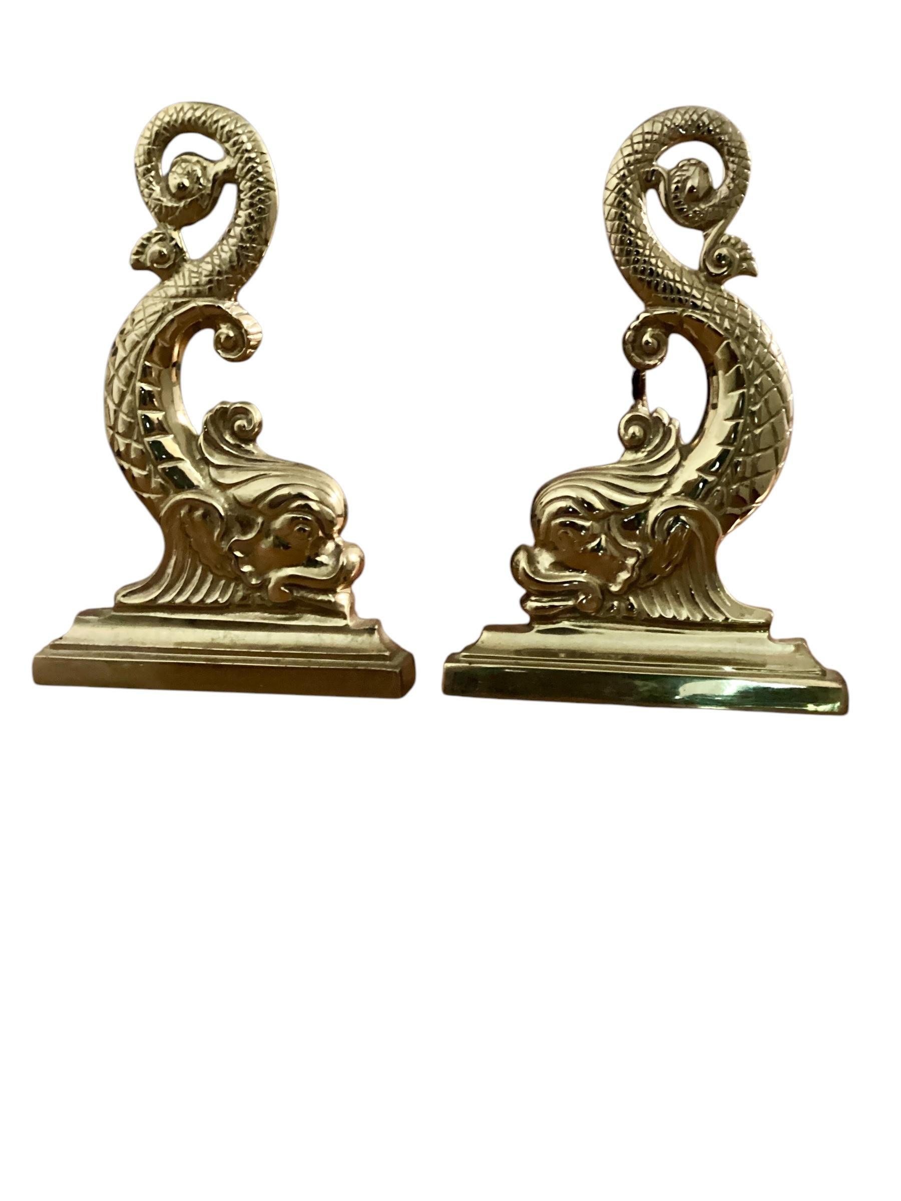 Pair of Brass Dolphin Andirons by Virginia Metalcrafters. Fully formed dolphin figures on a stepped base. The log holders also has brass dolphin finials. In good vintage condition with some evidence of prior fireplace use evident.