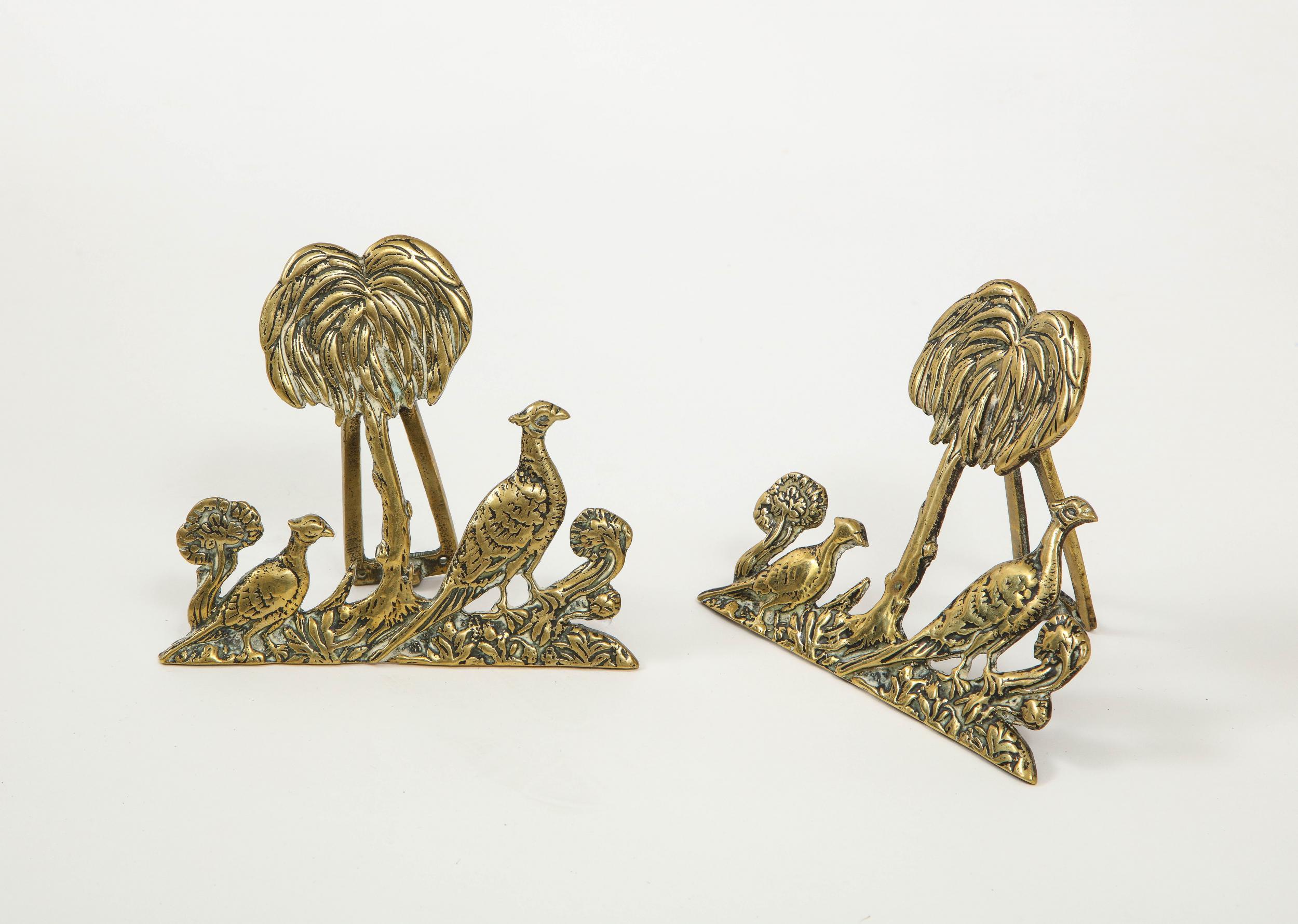 A pair of brass decorative objects, possibly door knockers, on a hinge or stand. Design of palm trees and birds.