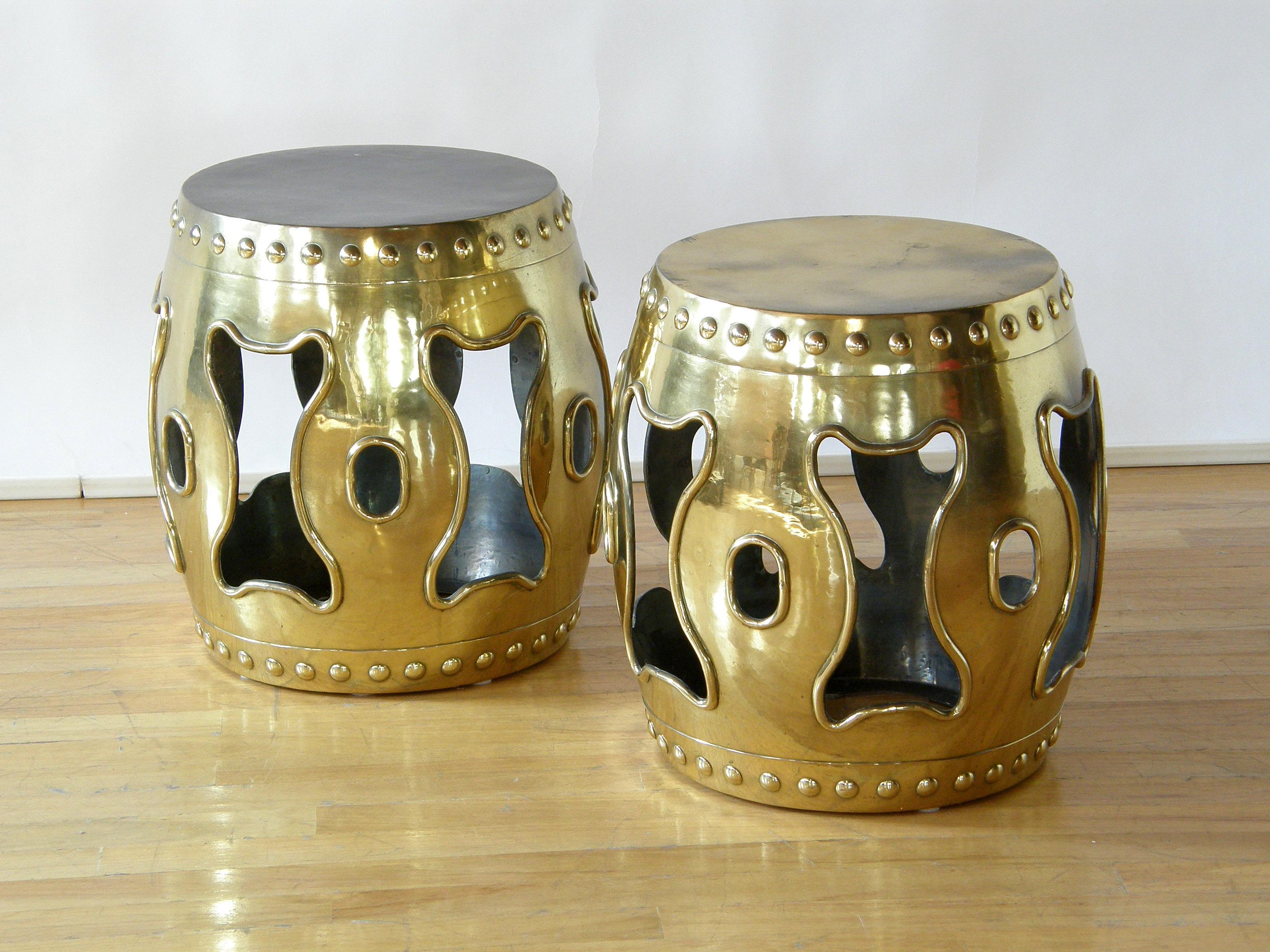 This pair of brass garden stools are designed after traditional Chinese garden stools. The shape imitates a Chinese drum with decorative, faux nailheads edging the top and bottom to simulate the attachment of the drumheads. The piercings on the