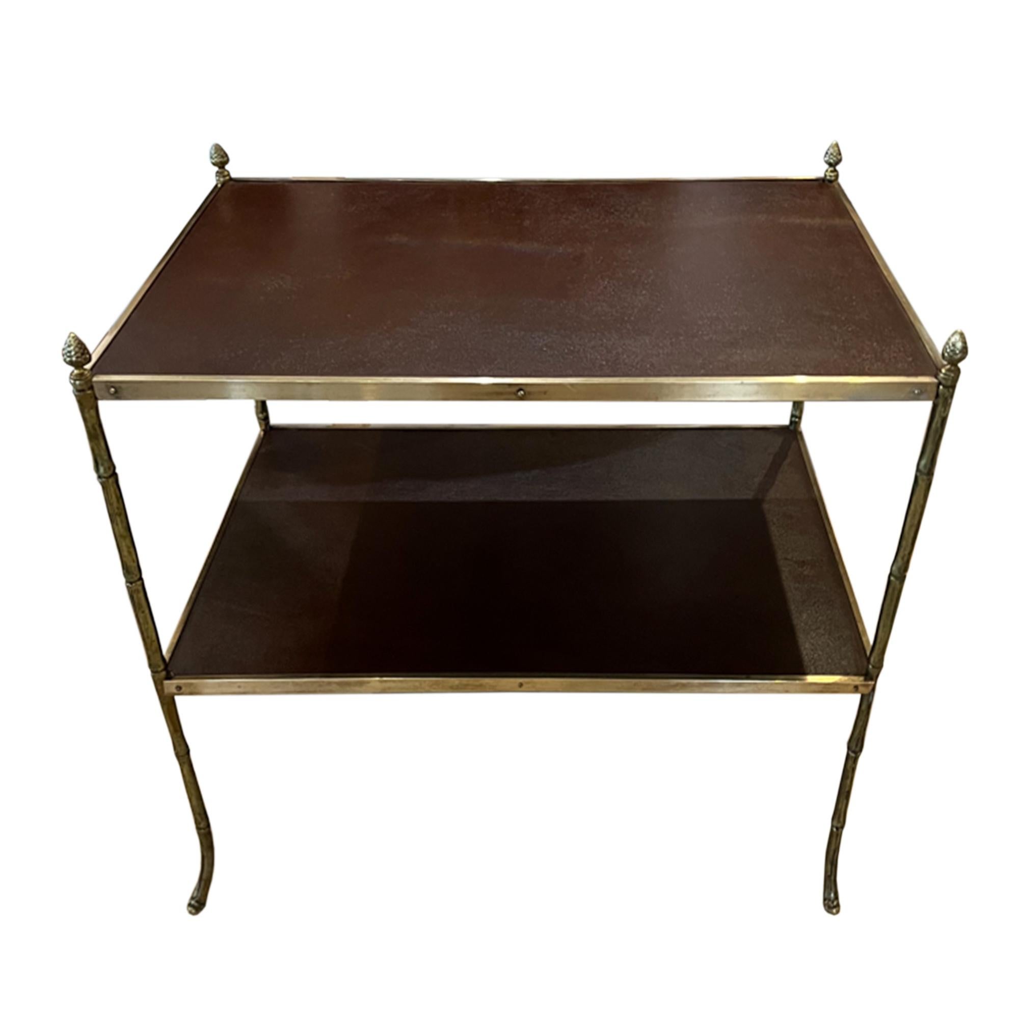 This pair of mid century side tables were made in France in the 1950s.

Made from brass using a faux bamboo design with elegant, sweeping legs, brown leather tops and pine cone finials. 

The height of the top shelf is 56cm and the lower shelf