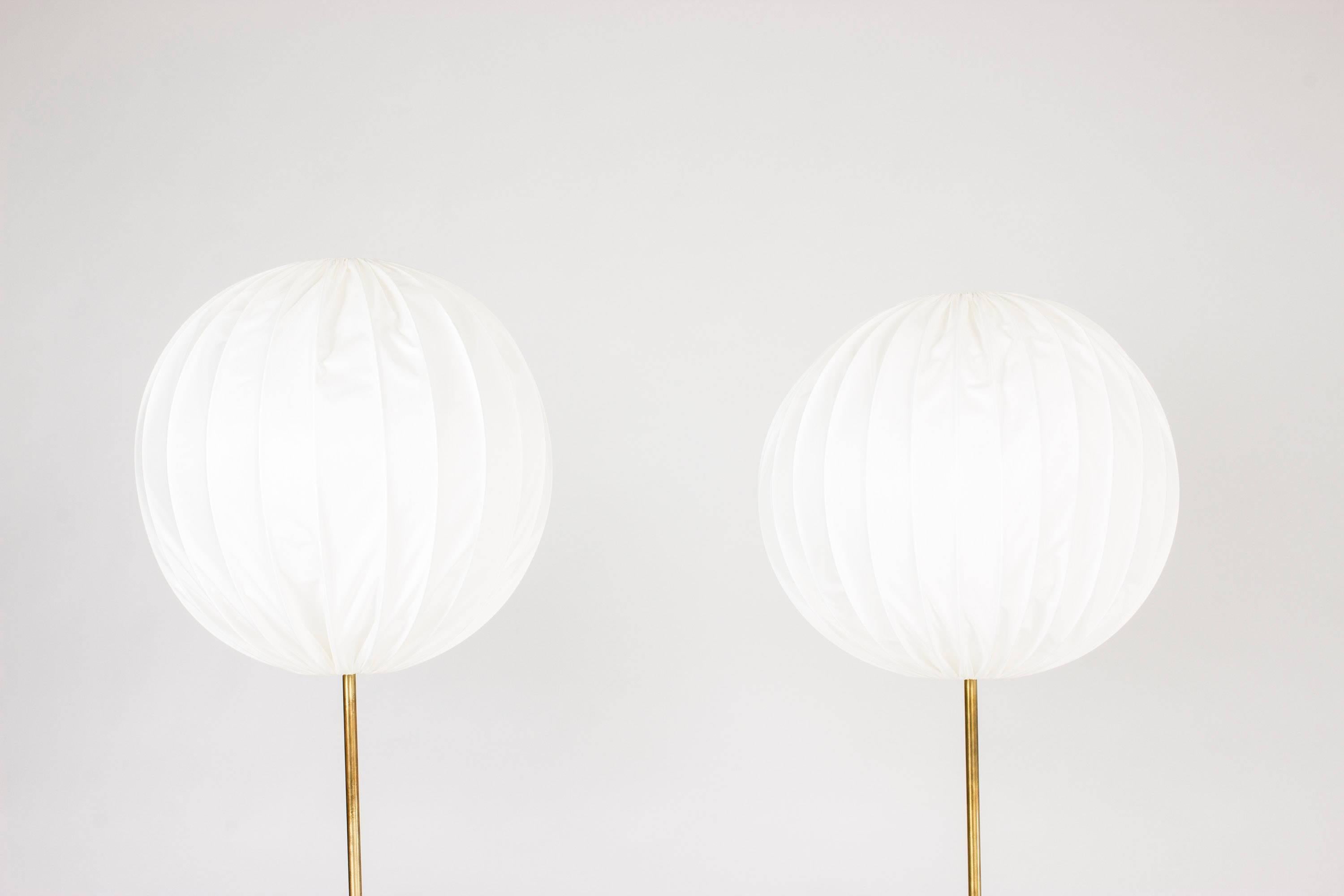 Stunning pair of floor lamps by Hans-Agne Jakobsson with chunky brass bases, slender handles and large round shades. Shades made from textile on metal wire frames.

Measure: Height 133 / 129 cm.