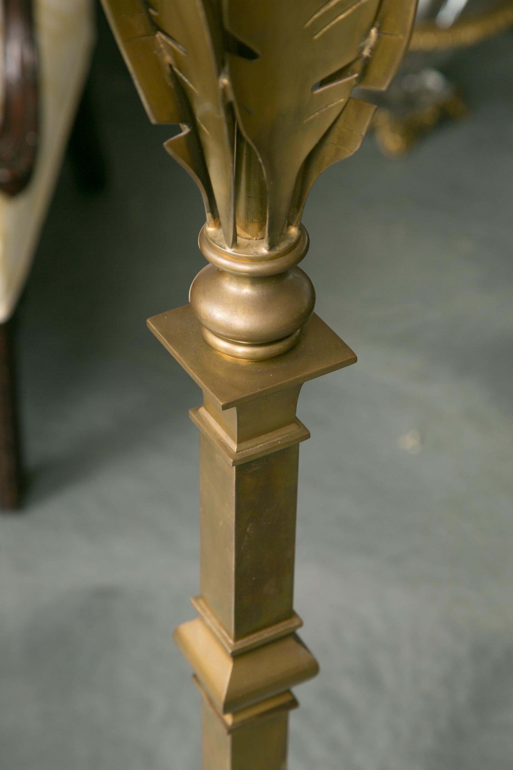 This is a pair of sophisticated brass floor lamps with stylized banana leaves atop a square stem situated on a prominent ogee shaped base on a square platform, circa late 20th century.