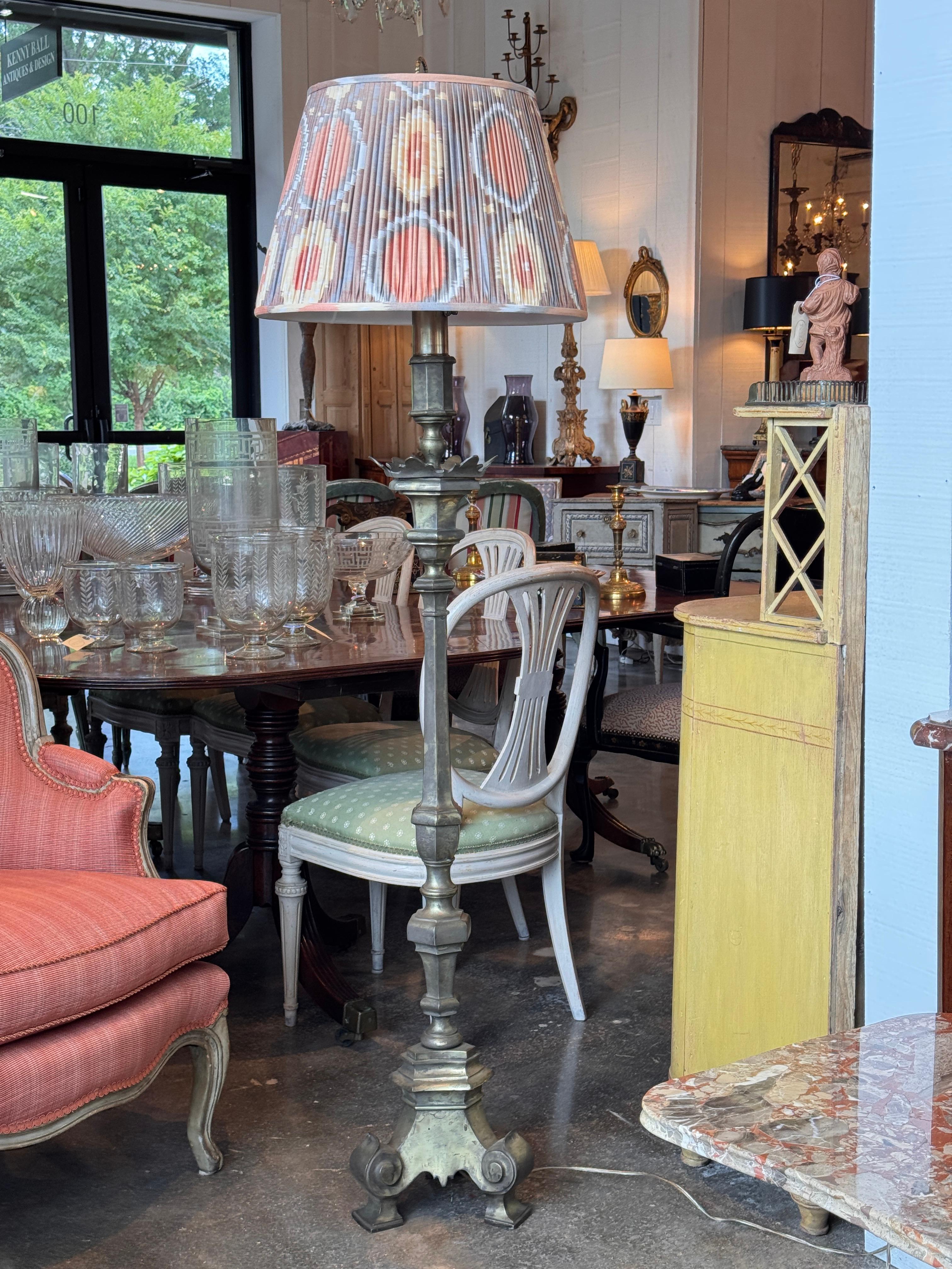Pair of tall brass floor lamps with hexagonal columns and finely cast tripod bases. The stepped and scrolled feet add architectural presence, while the aged patina enhances the sculptural silhouette. Shown with contemporary patterned shades.
