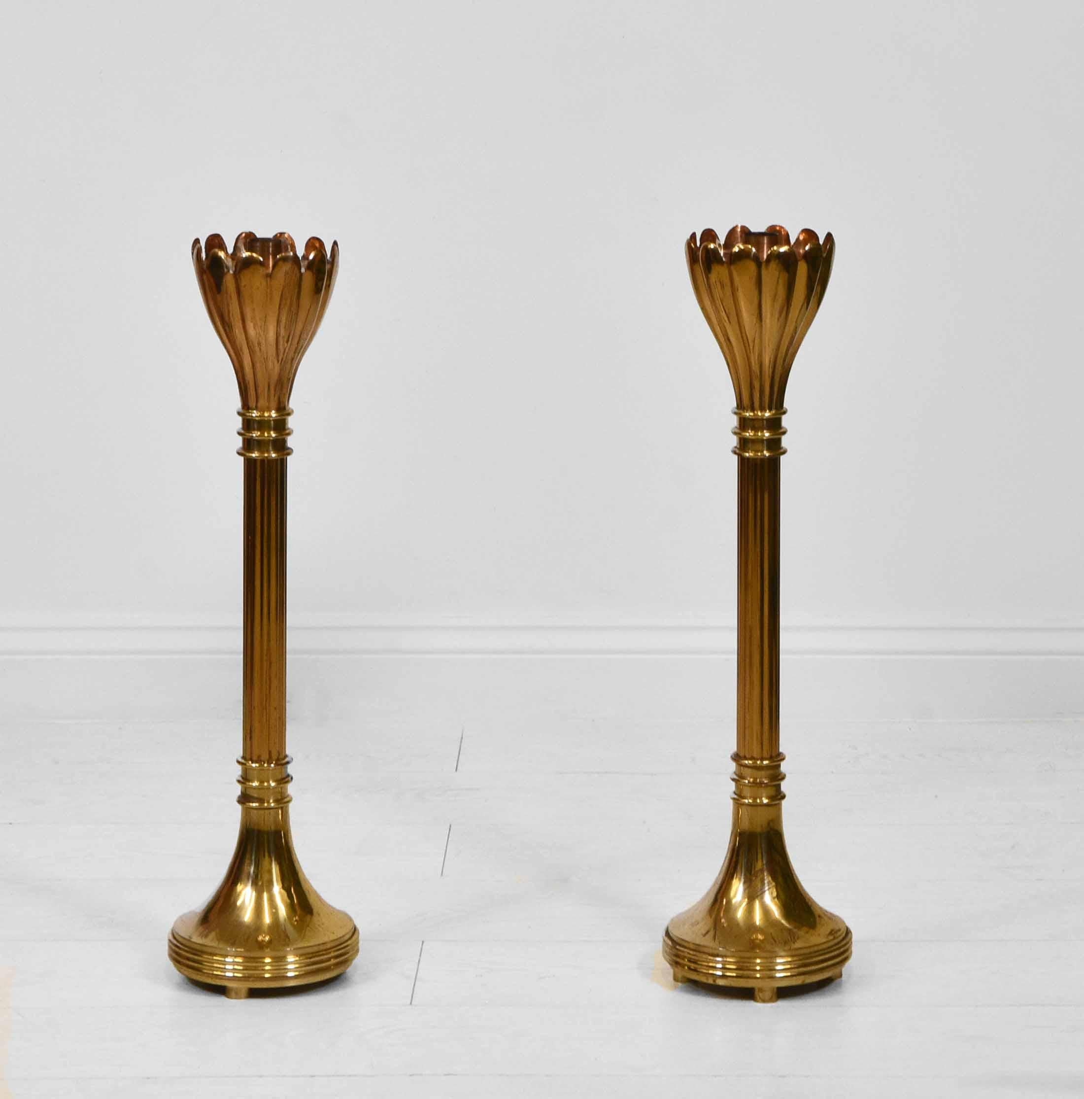 A pair of brass fluted floor standing candle stands with flared scalloped uppers. Circa early to mid 20th century.

The candle stands are made of brass, one having copper inset the other brass to the tops, They have weighted bases, each one weighing