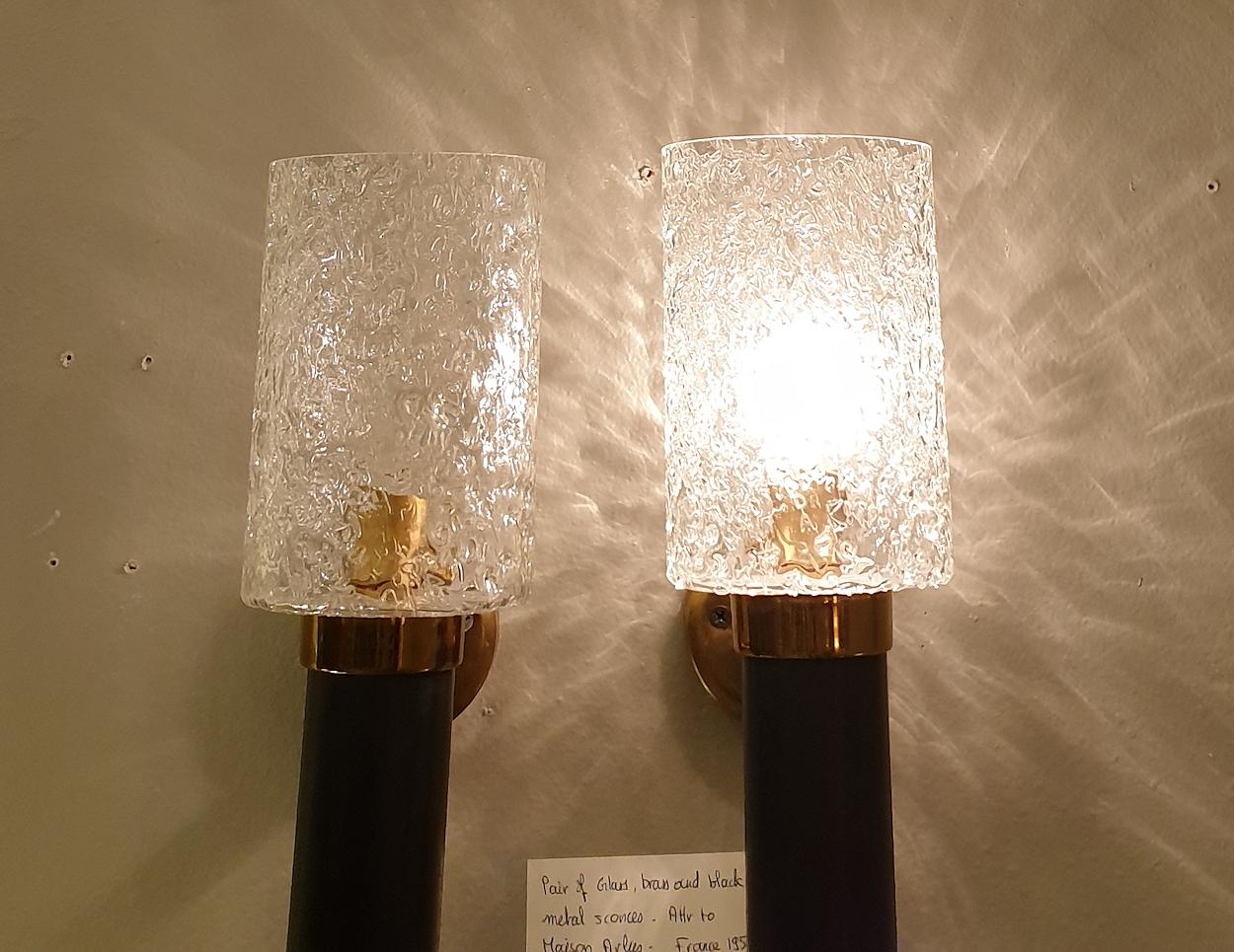 Pair of small Mid-Century Modern sconces, attributed to Maison Arlus, France, 1950s.
Made of a textured clear and translucent glass tube shade, hiding one light bulb, a black enamel metal cylinder base, and brass mounts.
1 light each, rewired for