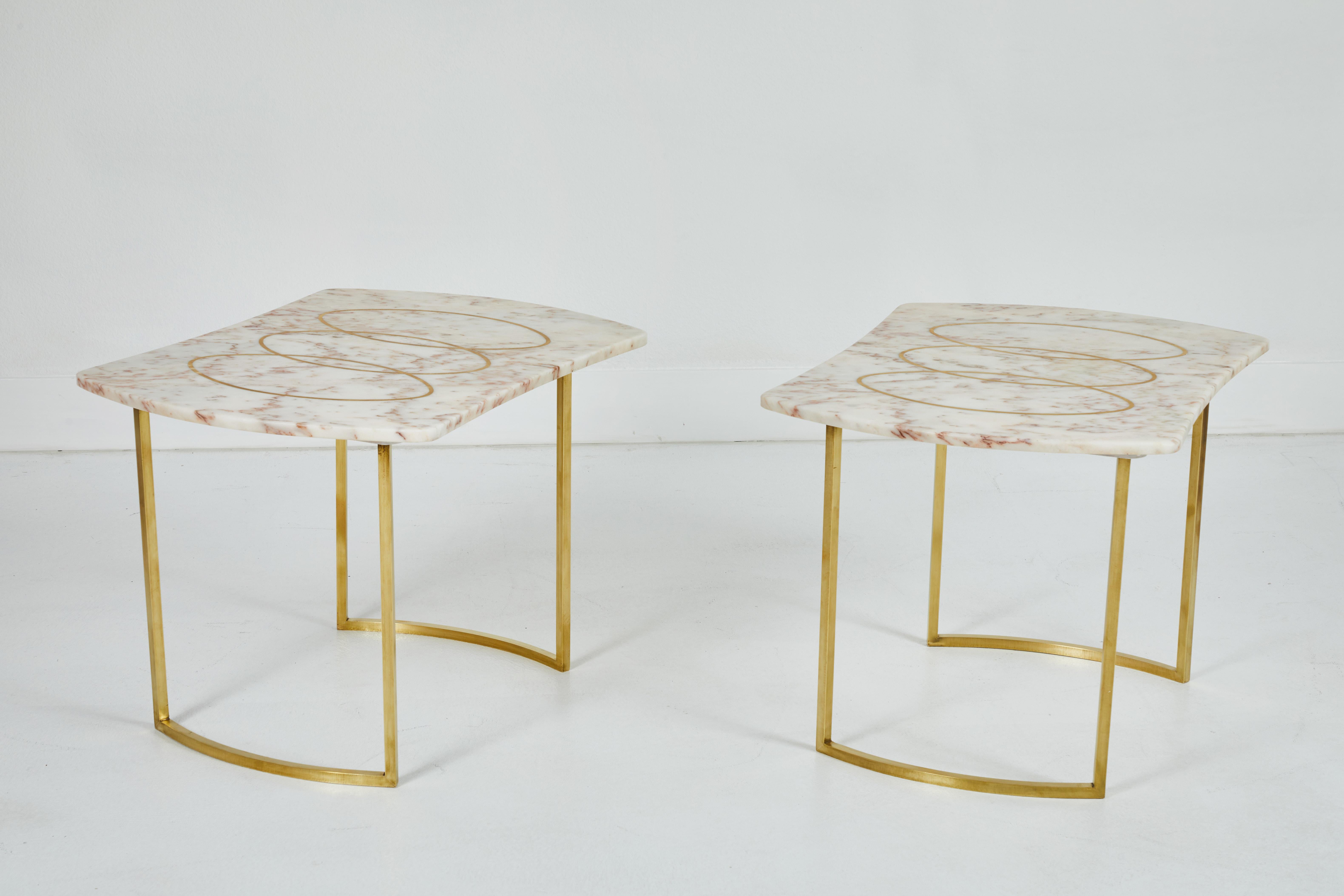 These are a pair of beautiful rose and cream colored marble top side tables. The tops are inlaid with 3 complimentary polished brass ovals overlapping each other. The bases are polished matching the inlay. These are perfect for beside a bed or as