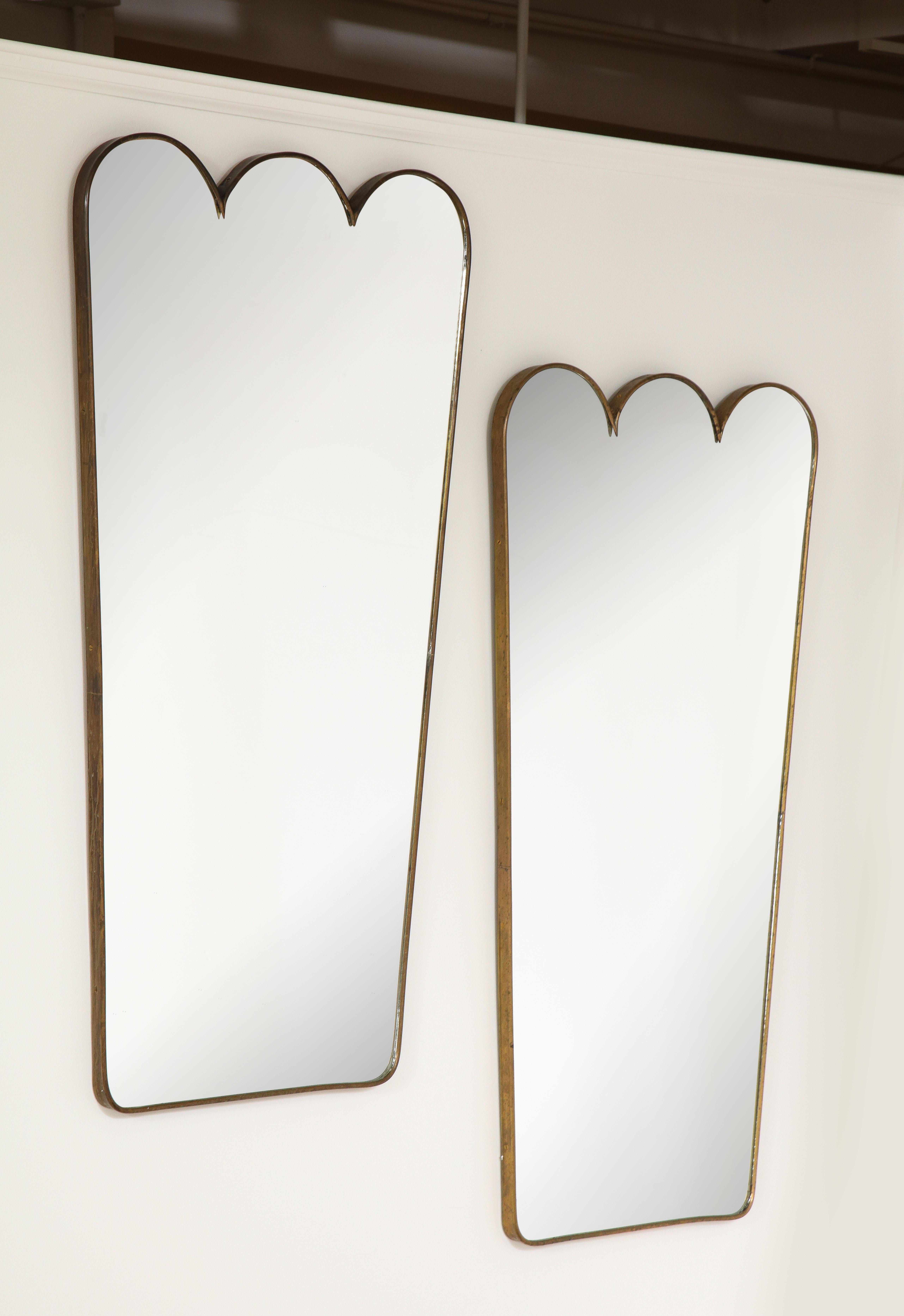 An elegant pair of Italian 1950's brass modernist mirrors with a scalloped shaped designed crest. Made with excellent craftsmanship and solid construction, with solid wood backing. This pair of mirrors offers clean modernist lines and of organic