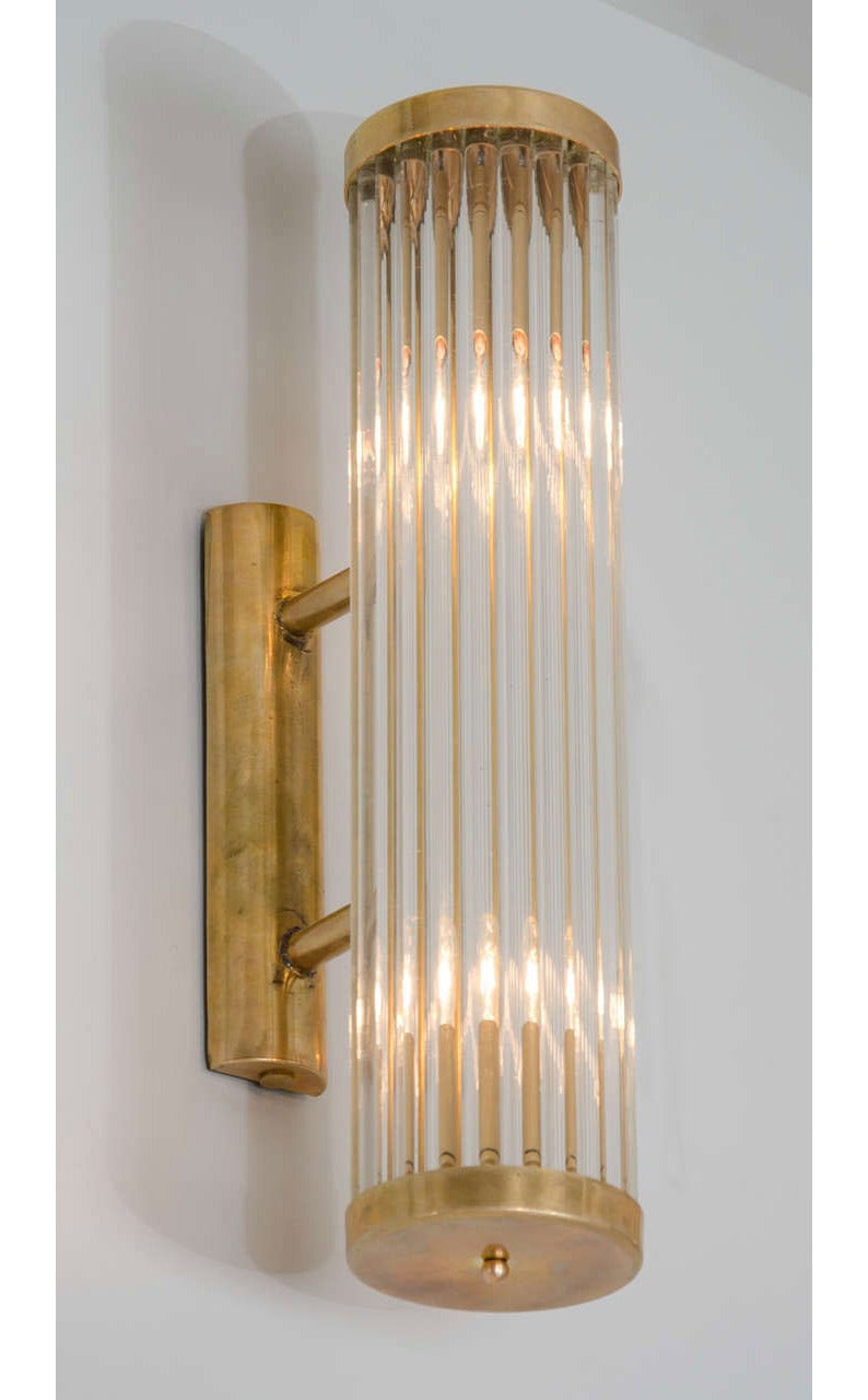Contemporary Art Deco inspired Italian wall lights in the style of ‘Venini’.
Each light comprises of a circle of slim Murano glass rods capped top and bottom by round brass plates that attach with two slim brass arms to a brass wall bracket.
Two