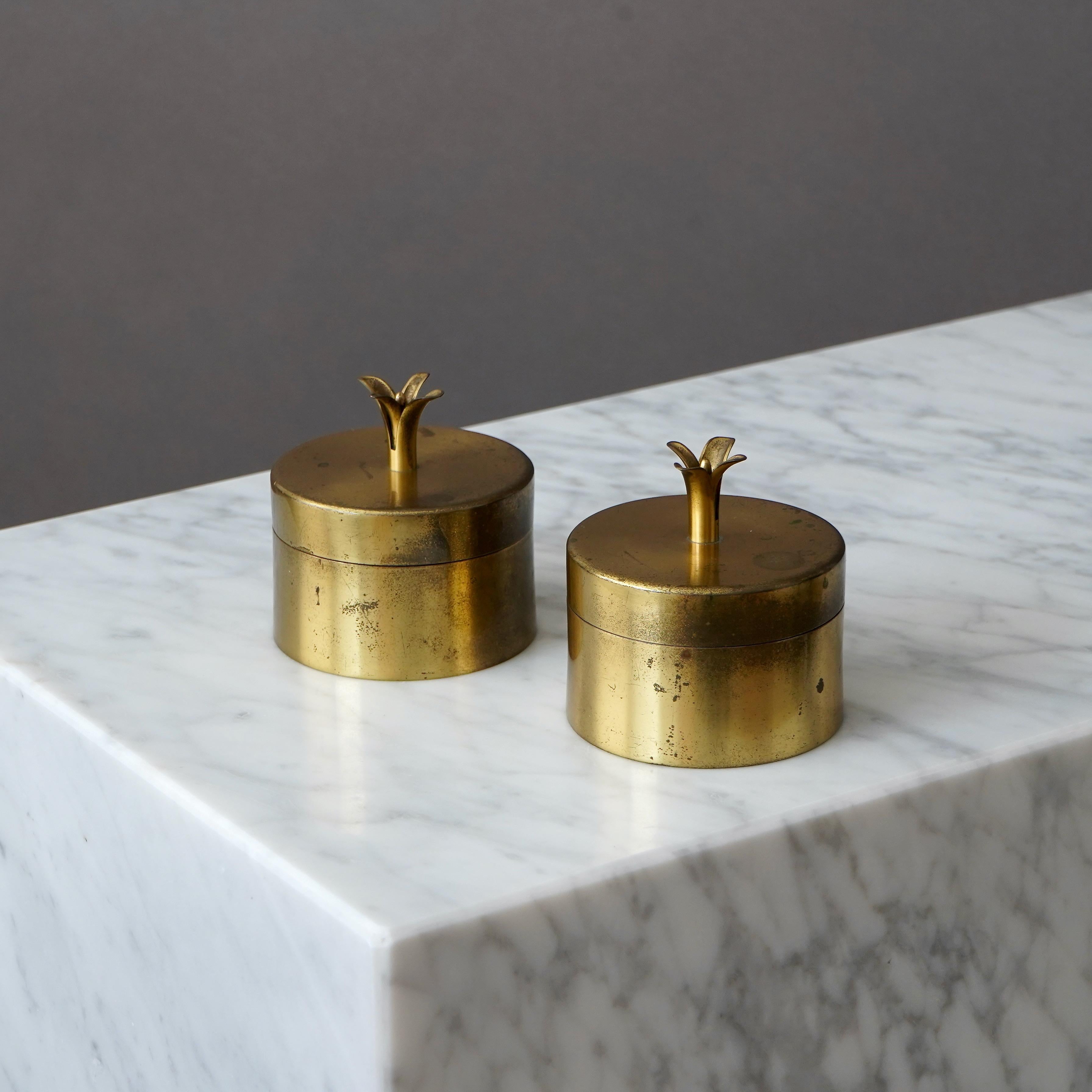 A pair of beautiful brass jars with amazing patina. Inside with glass inserts. The lid adorned with a knob in the shape of a lily (just like the famous 'Liljan' candle holders). 

Designed by Ivar Ålenius Björk for Ystad Metall, Sweden,