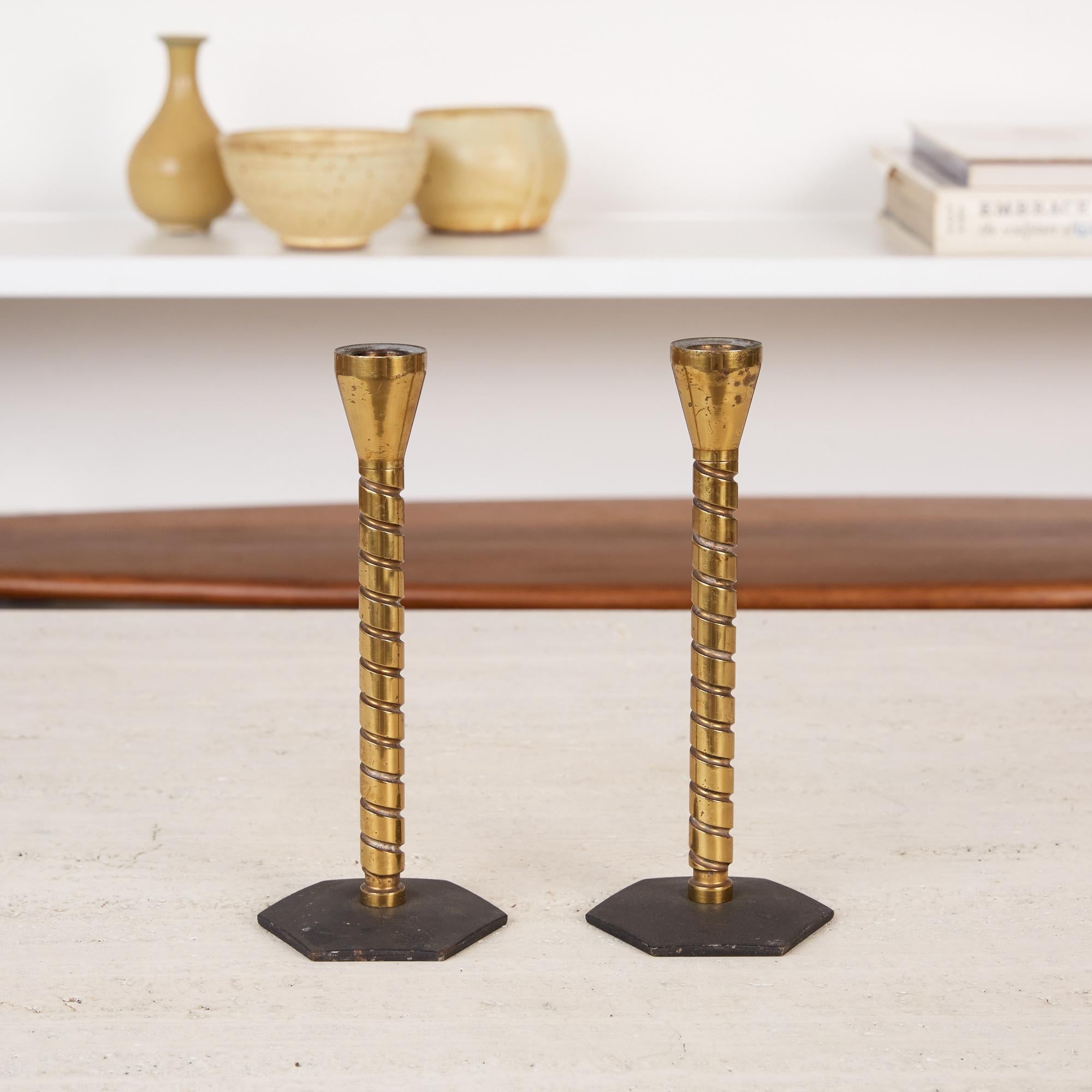 Pair of brass Machine Age candlesticks. The pair of patinated brass candlesticks feature threaded stems with thick grooves and blackened steel hexagonal bases. The Industrial Design works in a multitude of interior styles.

Dimensions: 3” width x