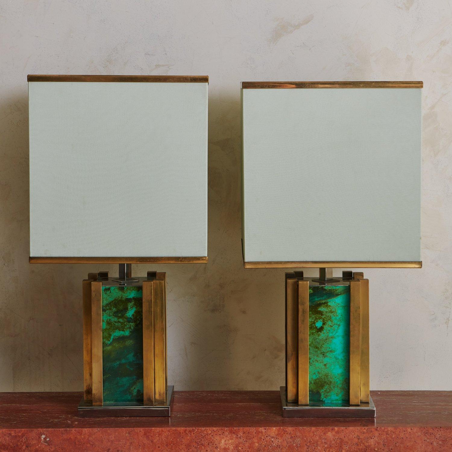 A pair of Mid Century Italian table lamps designed by Romeo Rega. These lamps feature architectural bases constructed with patinated brass and glass with a captivating green marbled effect. They have square chrome platforms and retain their original