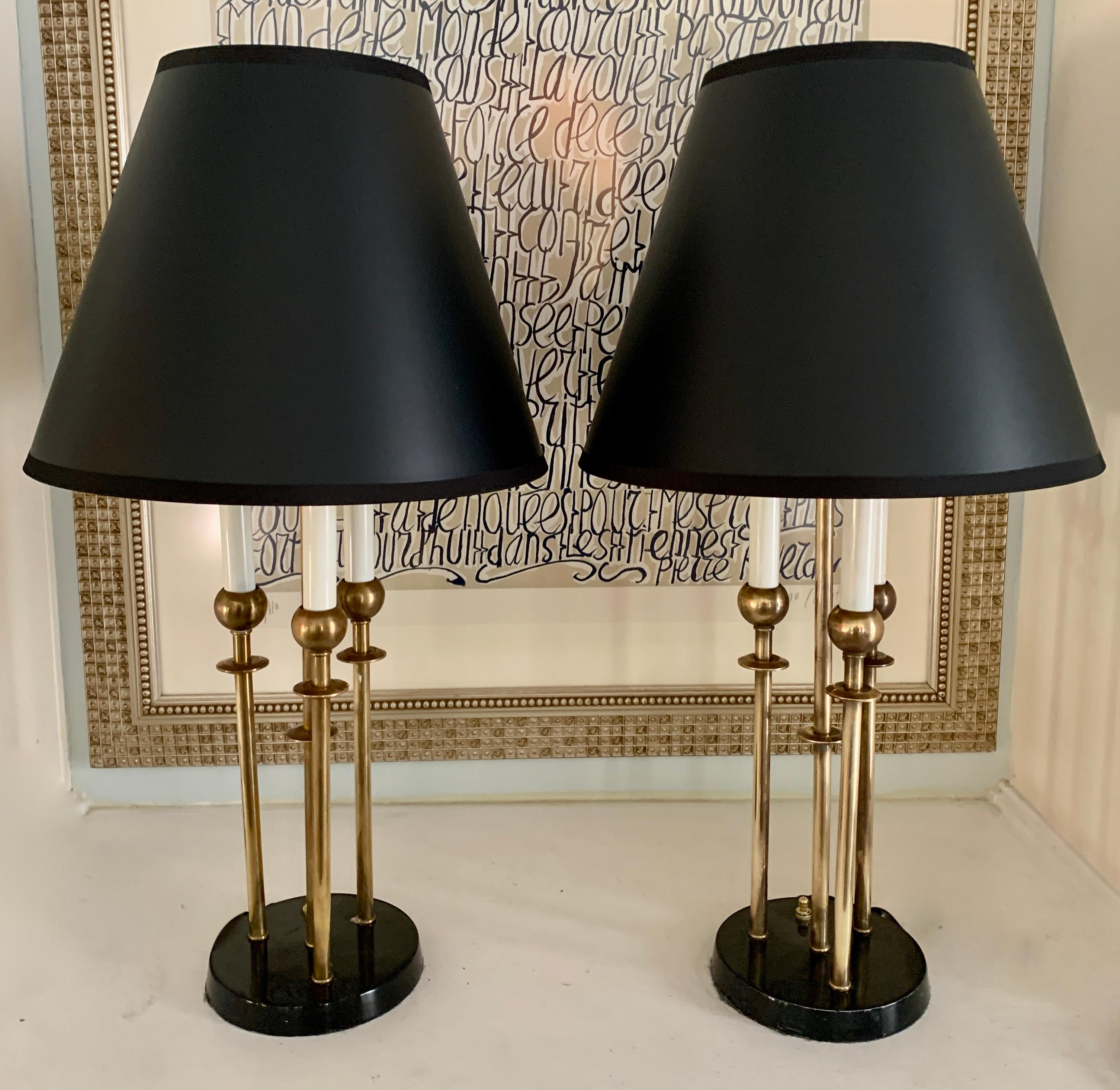 A pair of brass lamps with three brass candlesticks, and midcentury detailing. The lamps come with shown black shades and have been rewired with 6' silk cords. A complement to any living room, bedroom or guest room.

Shades are cone shaped and 7
