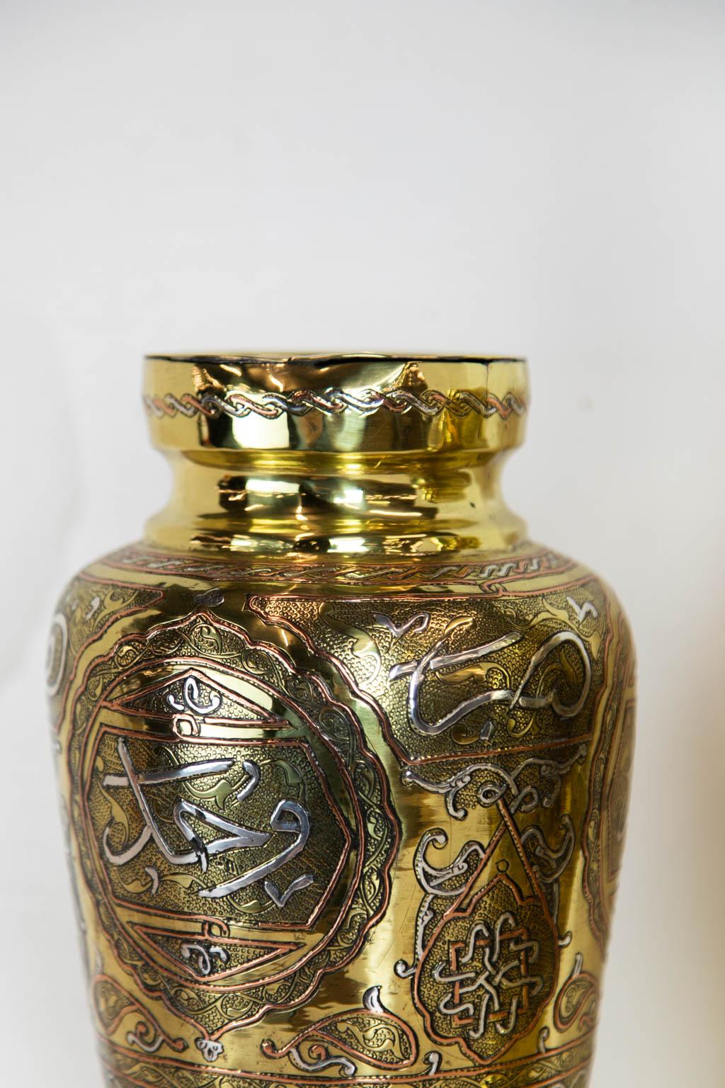 This pair of brass, silver, and copper vases is engraved with multiple cartouches that have a stipled background, framed, and overlaid with silver and copper ornamentation. They are polished and lacquered for ease of maintenance.