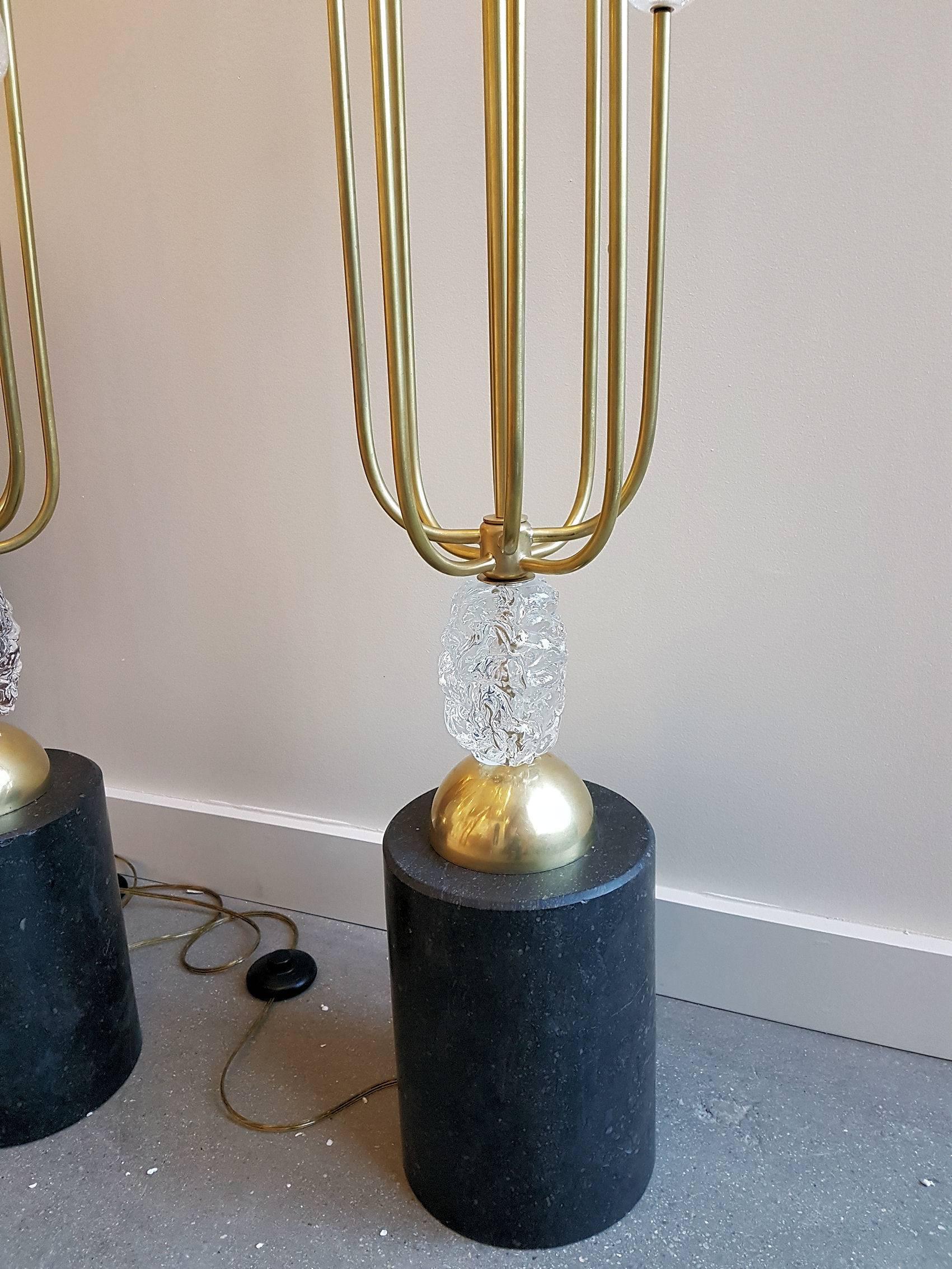Pair of Mid-Century Modern standing floor lamps.
The cylindrical base is in black veined stone.
Eight branches of brass hold a Murano Pulegoso plain glass egg: Pulegoso is a Murano glass technique: a type of glass characterized by countless