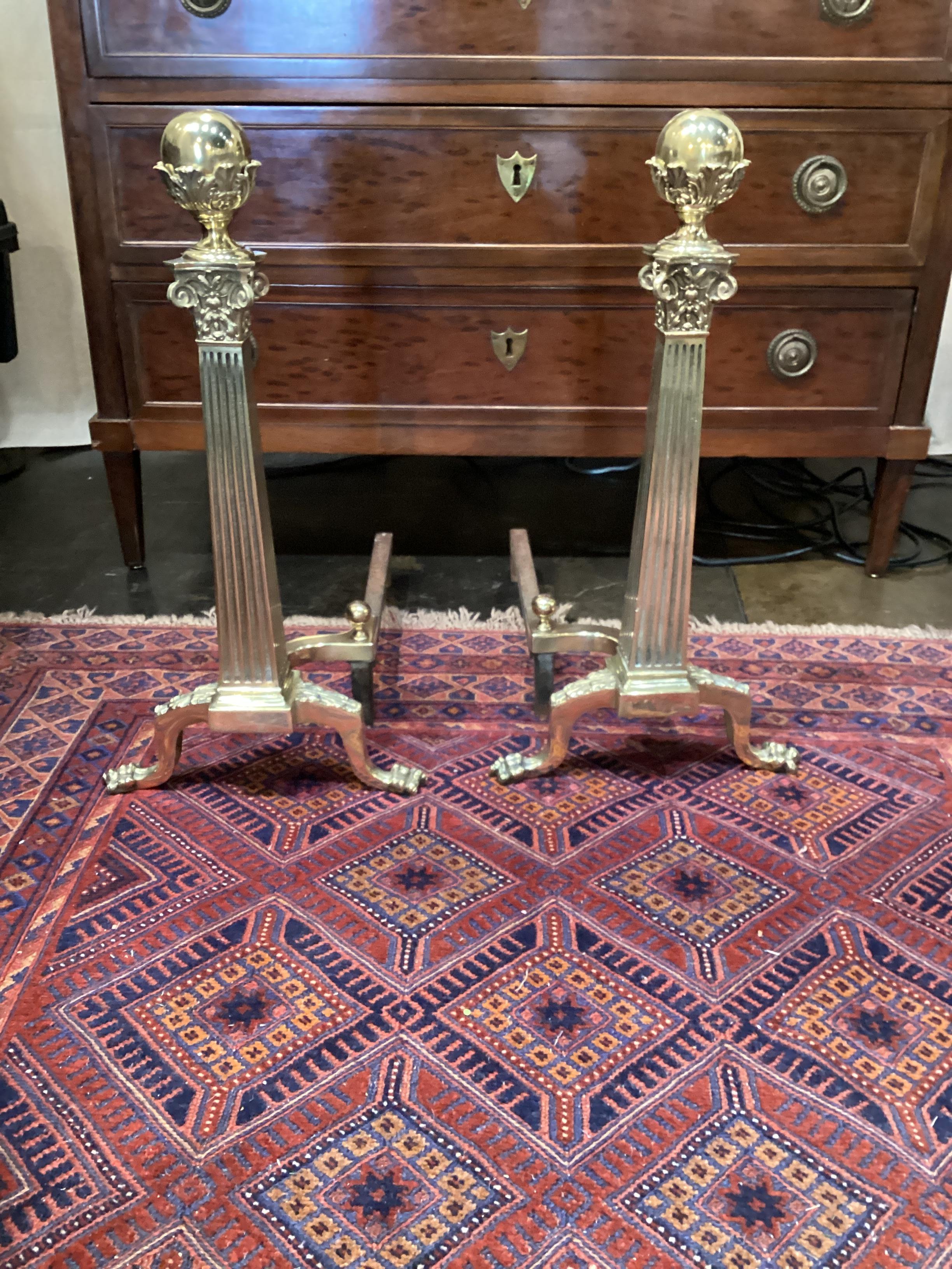 Pair of Brass Neoclassical Style Andirons. Square tapering reeded column with corinthian capitals resting on splayed paw feet.