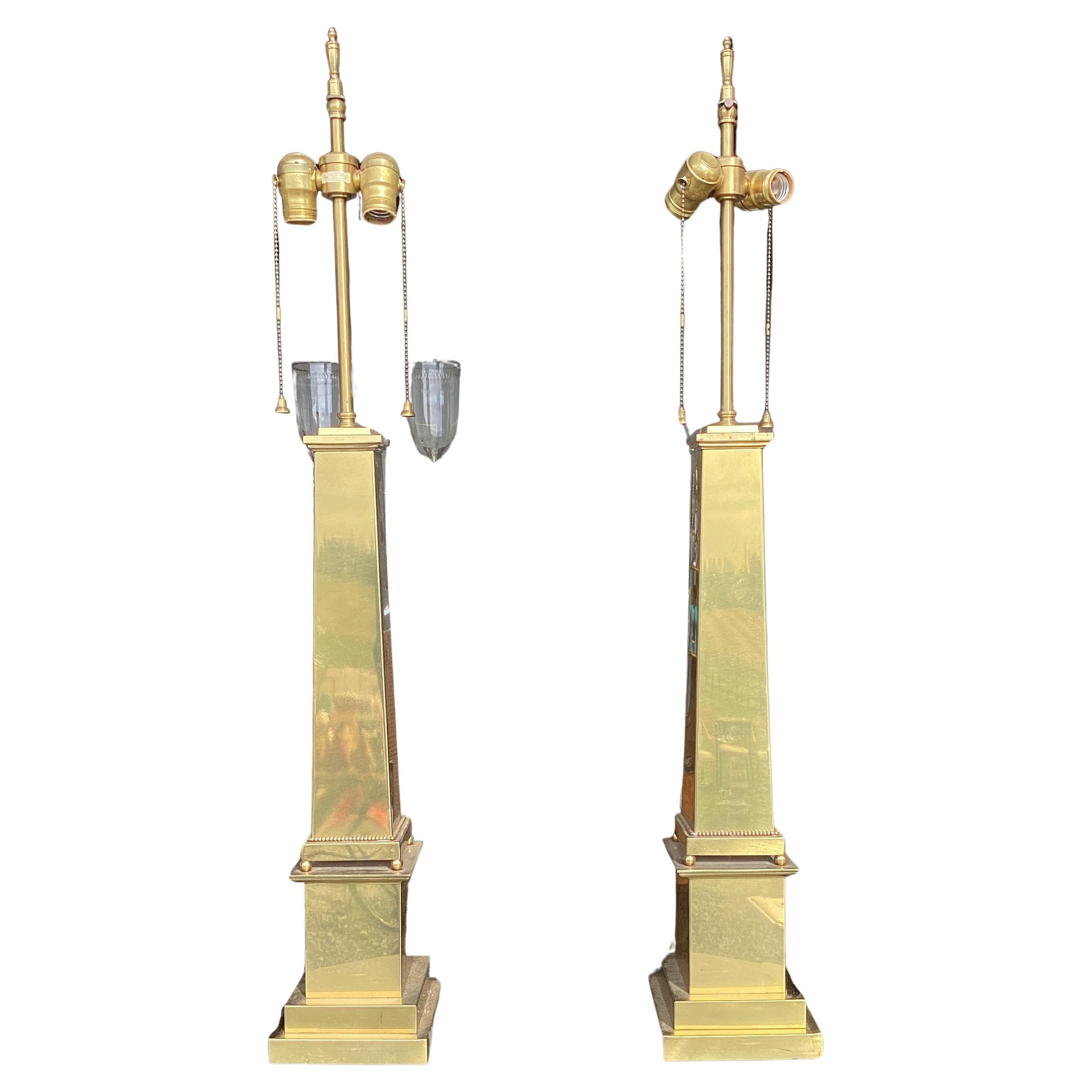 Pareja de lámparas de sobremesa en forma de obelisco de latón, de Warren Kessler. Forma clásica de obelisco con zócalo cuadrado y base escalonada. La columna cuadrada descansa sobre una bola redonda. Las lámparas están conectadas con un doble grupo