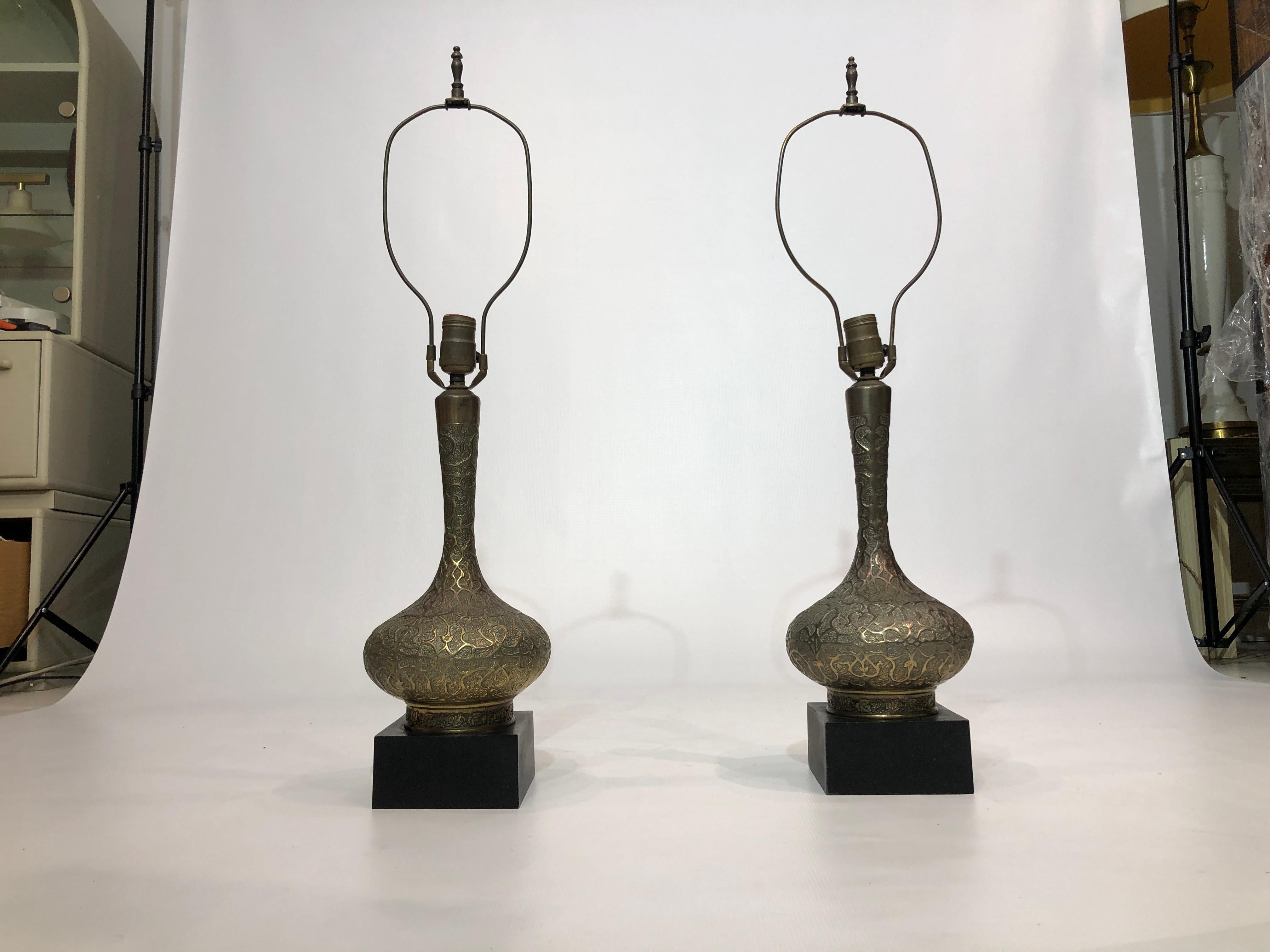Pair of oriental style table lamps in bass embossed and patinated body and black metal base. The brass body has a beautiful orientalist revival design yet discrete, they would look amazing with the right shades and in a modern or vintage interior,