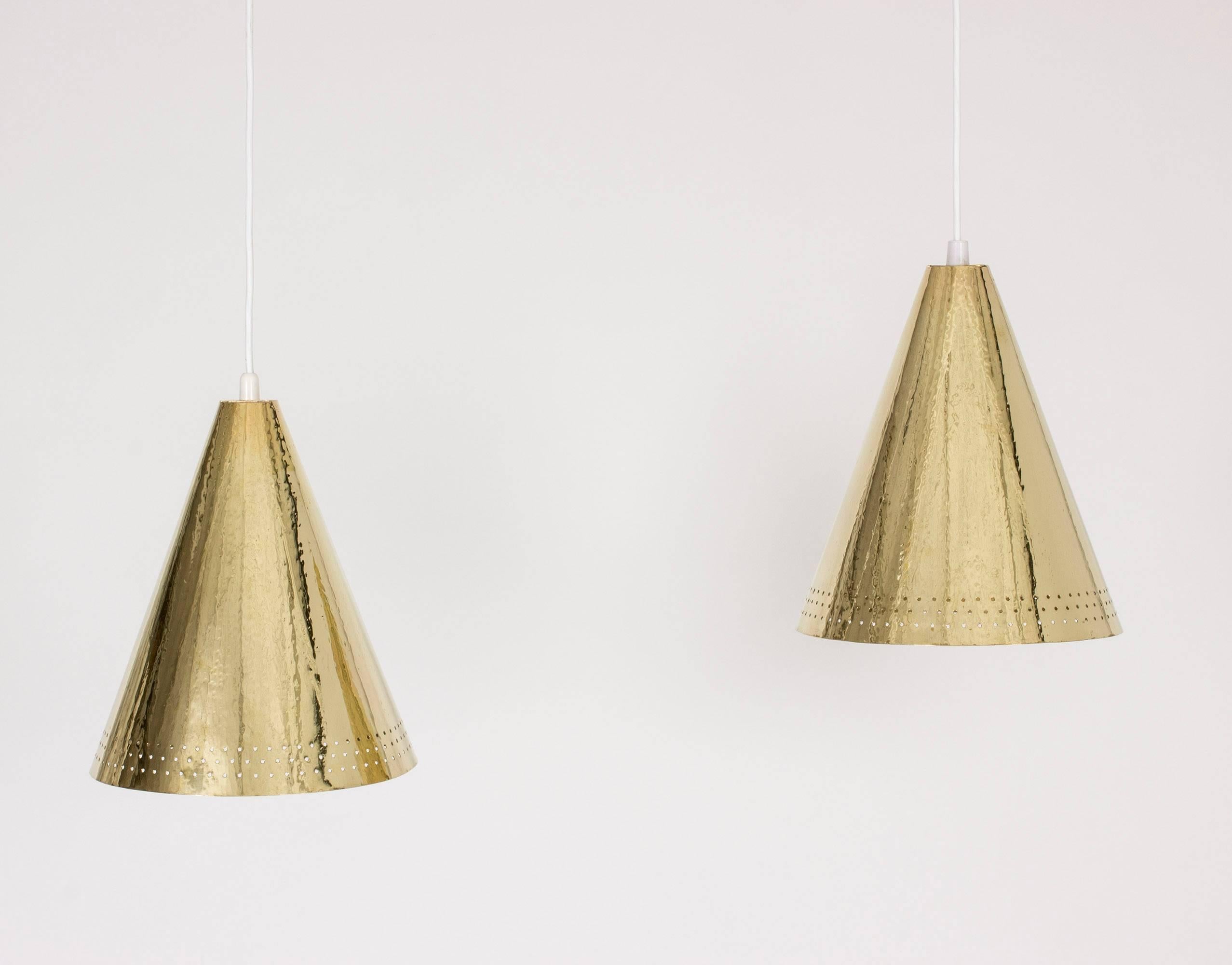 Pair of beautiful brass pendant lamps by Hans Holmström, with a hand-hammered finish that bring life and luxury to the simplistic silhouettes. The shades are perforated with a pattern of holes around the bottom edge.