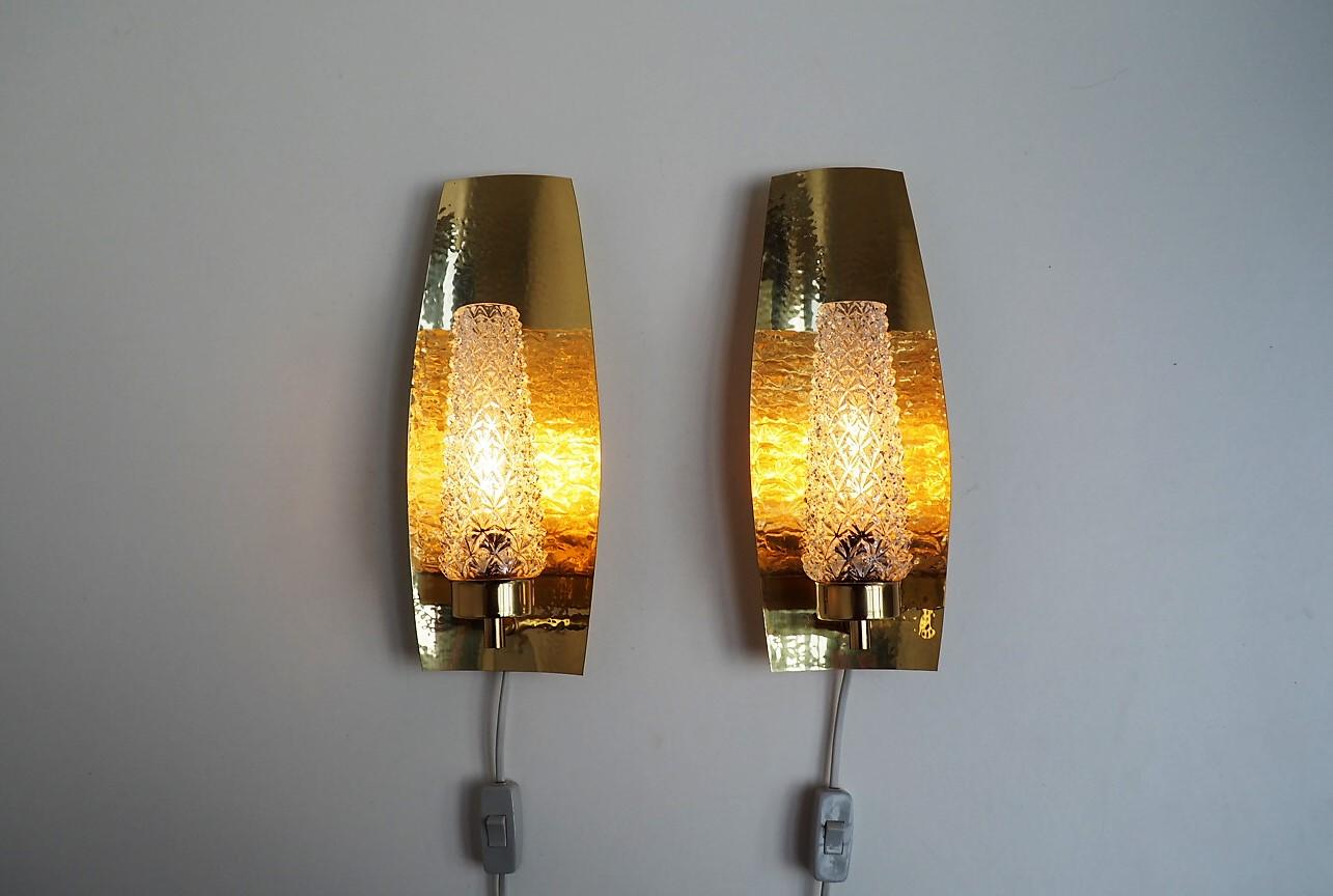 Pair of large sconces with wall base made in solid brass and to cover for the bulbs they have a decorative glass shade. They are made by a Scandinavian manufacturer during the 1960s.
The wall bases are designed with hammered brass which together