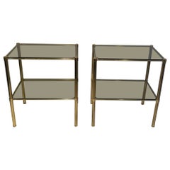 Pair of brass side tables with smoked glass shelves. French Work. Circa 1970