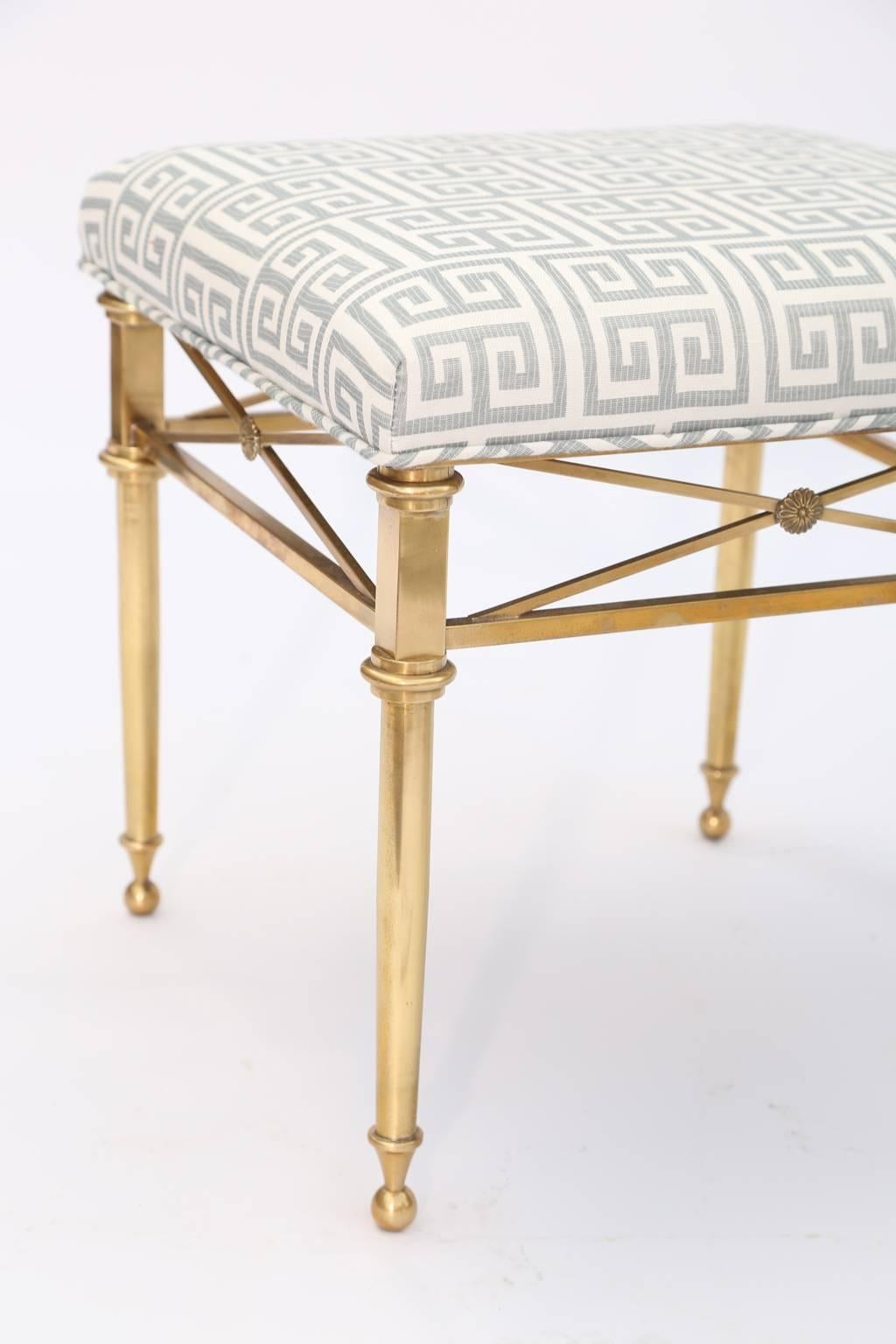 Pair of stools, each having a square upholstered crown seat, on frame of brass, raised on round, tapering legs, joined by box-stretcher, with cross decoration, centred with a rosette, ending in ball feet. 

Stock ID: D1636.