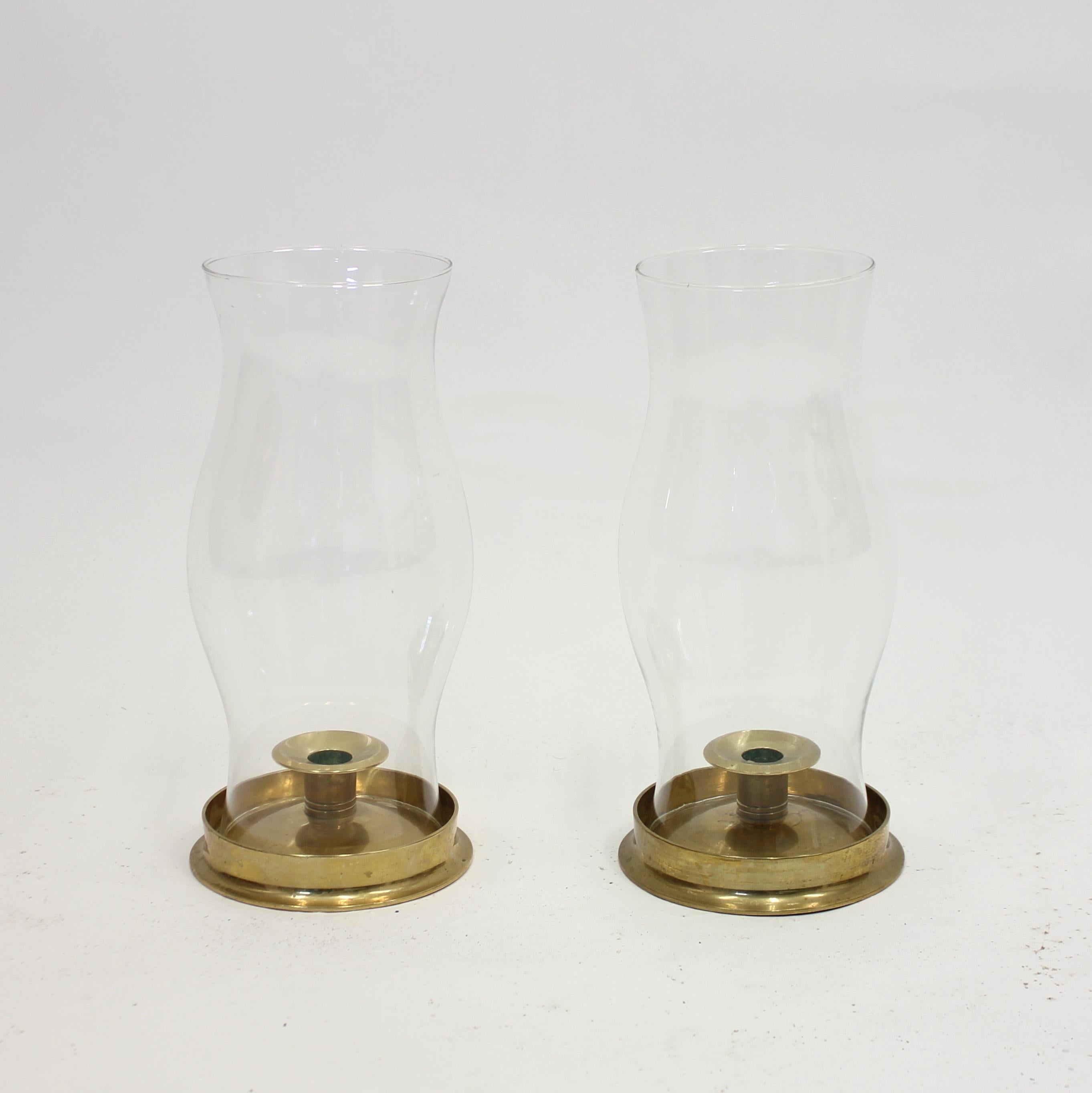 Pair of brass and glass storm lanterns or hurricane lamps / candle holders from ca 1970s. The glass is removable for an easy change of the candle light and has an organic shape that is a bit broader in the middle. Very good vintage condition with