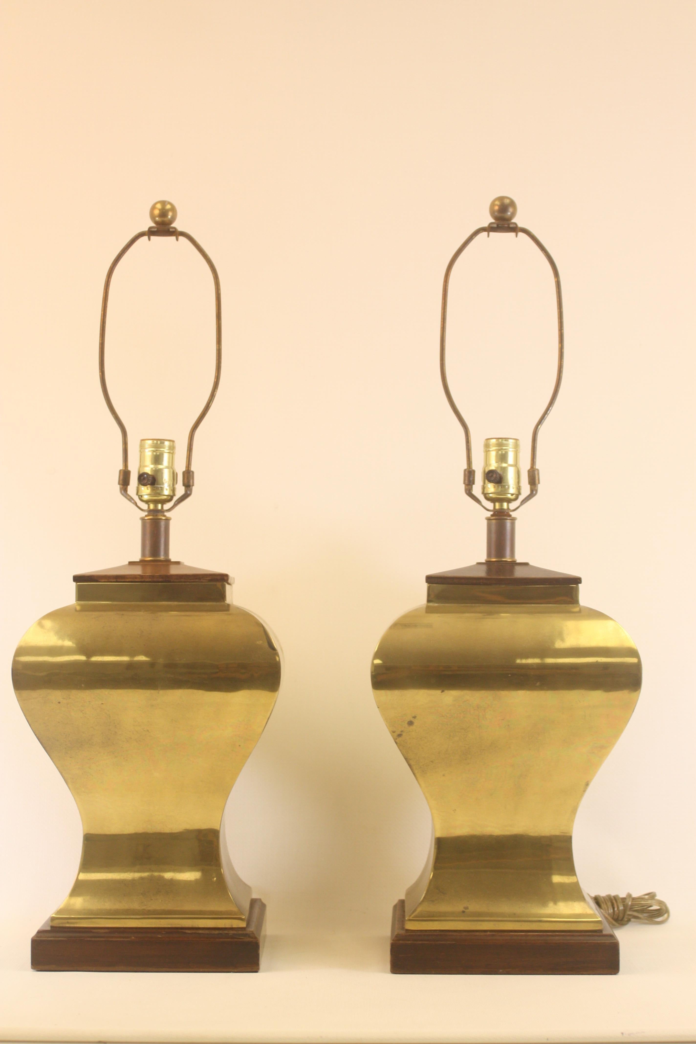 Pair of elegantly shaped brass and wood base lamps by Tyndale.  The total height to the tip of the finial is 26.5'' and the height to the bulb receptacle is: 18.5'' The width is about 9''.
These are very classical and would look great in a modern or