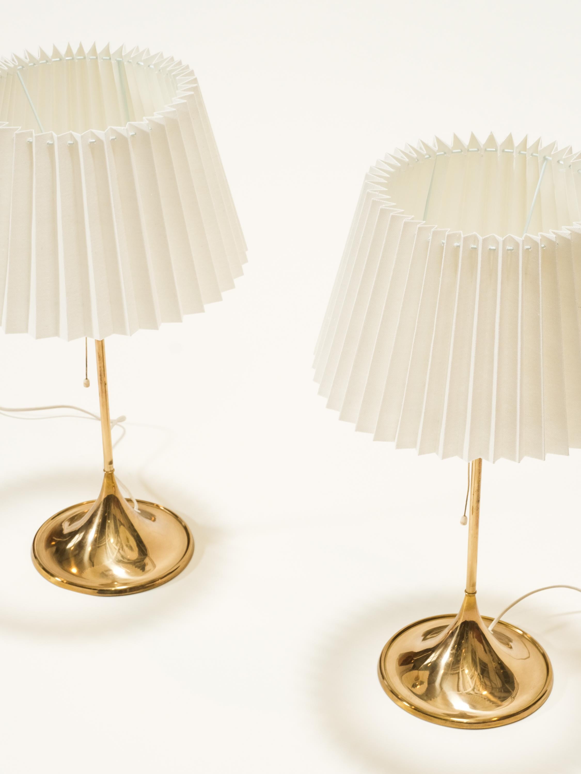 This pair of elegant table lamps was produced by Bergboms in Sweden in the 1960s. The model is numbered B-024.
The lamp consists of a polished brass stem and tulip shaped base and a new fabric shade. 

Marked on the bottom of the base by the