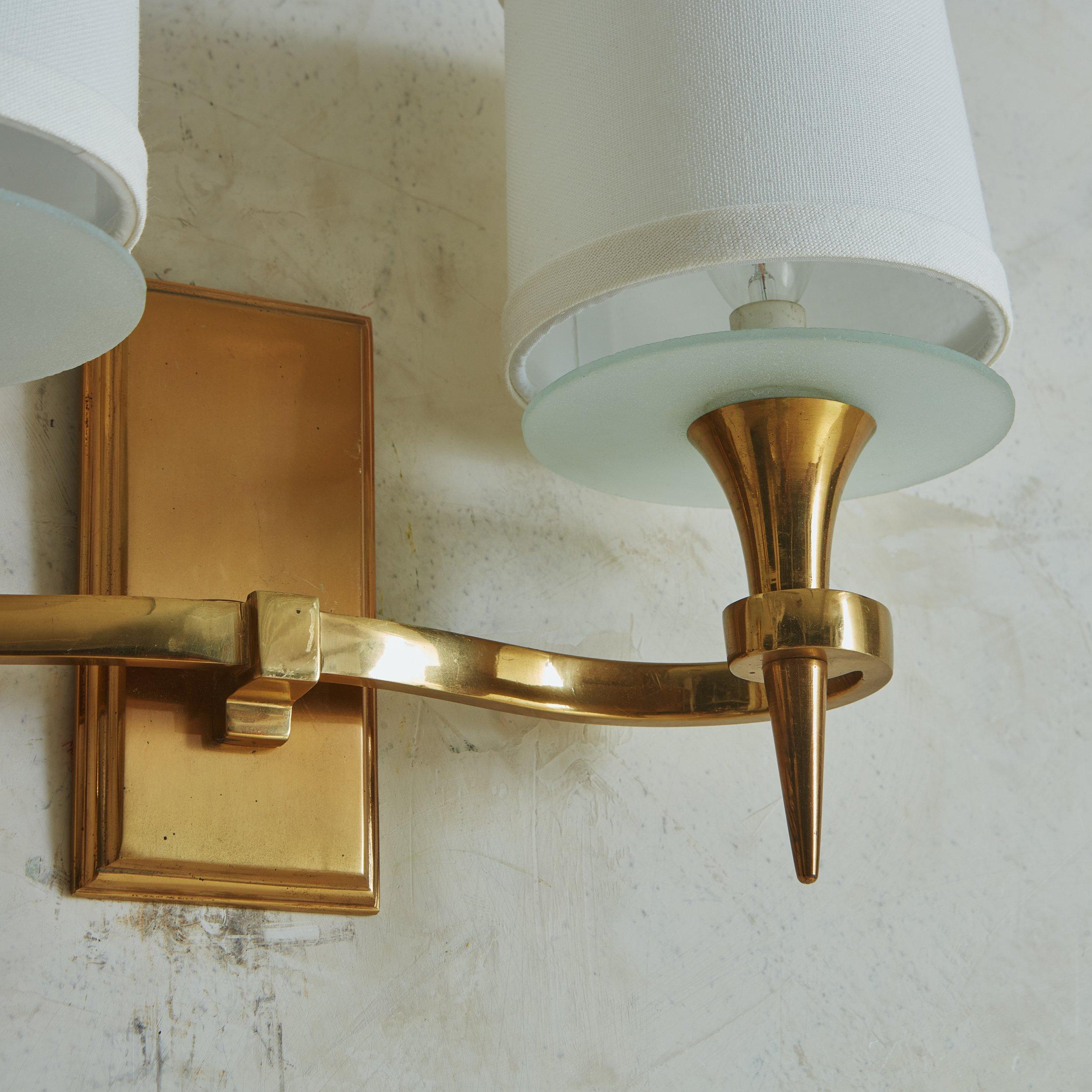 A pair of 1940s brass wall sconces featuring two beautifully curved arms with elegant cone shaped torches. They have rectangular backplates with a fine beveled edge, frosted glass bobeches and new white fabric shades. Unmarked. Sourced in France,