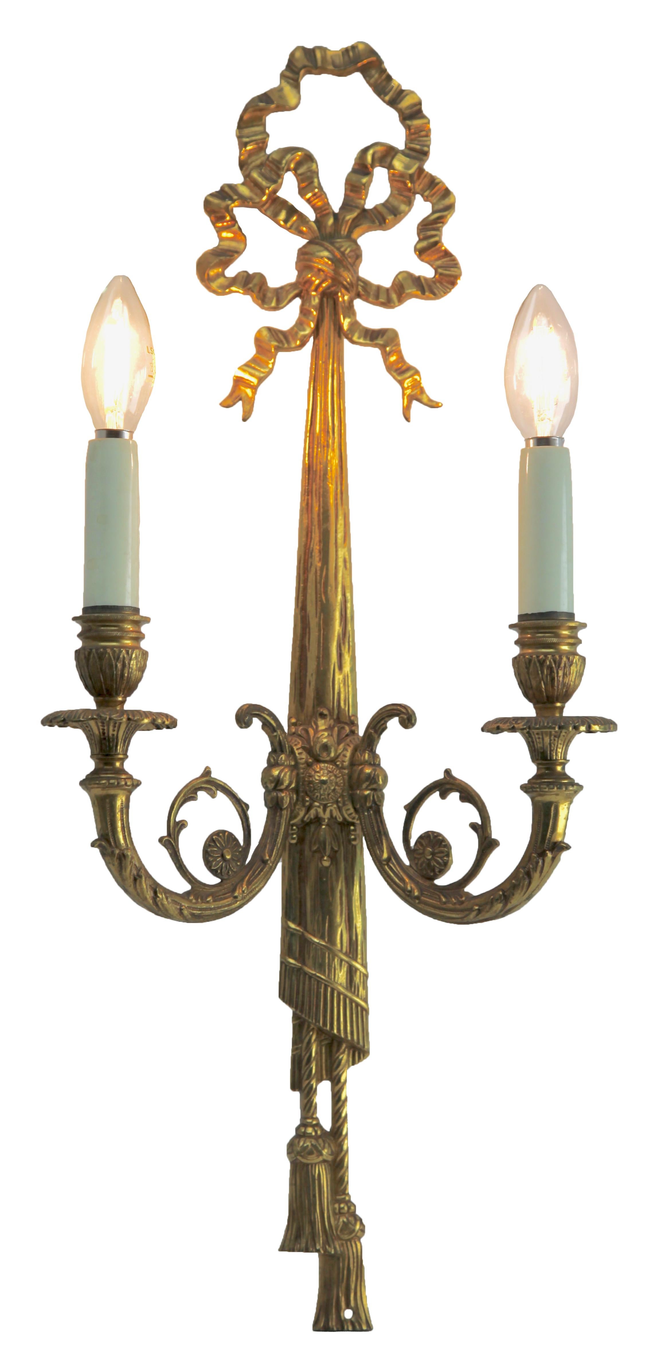 Pair of cast brass sconces (electroliers) in the Louis XVI style, each with two candle-fittings for electric lamps.
Decorated with ribbons and drapery with tassels and each having two arms with rococo scrolls and detail supporting a faux candle in
