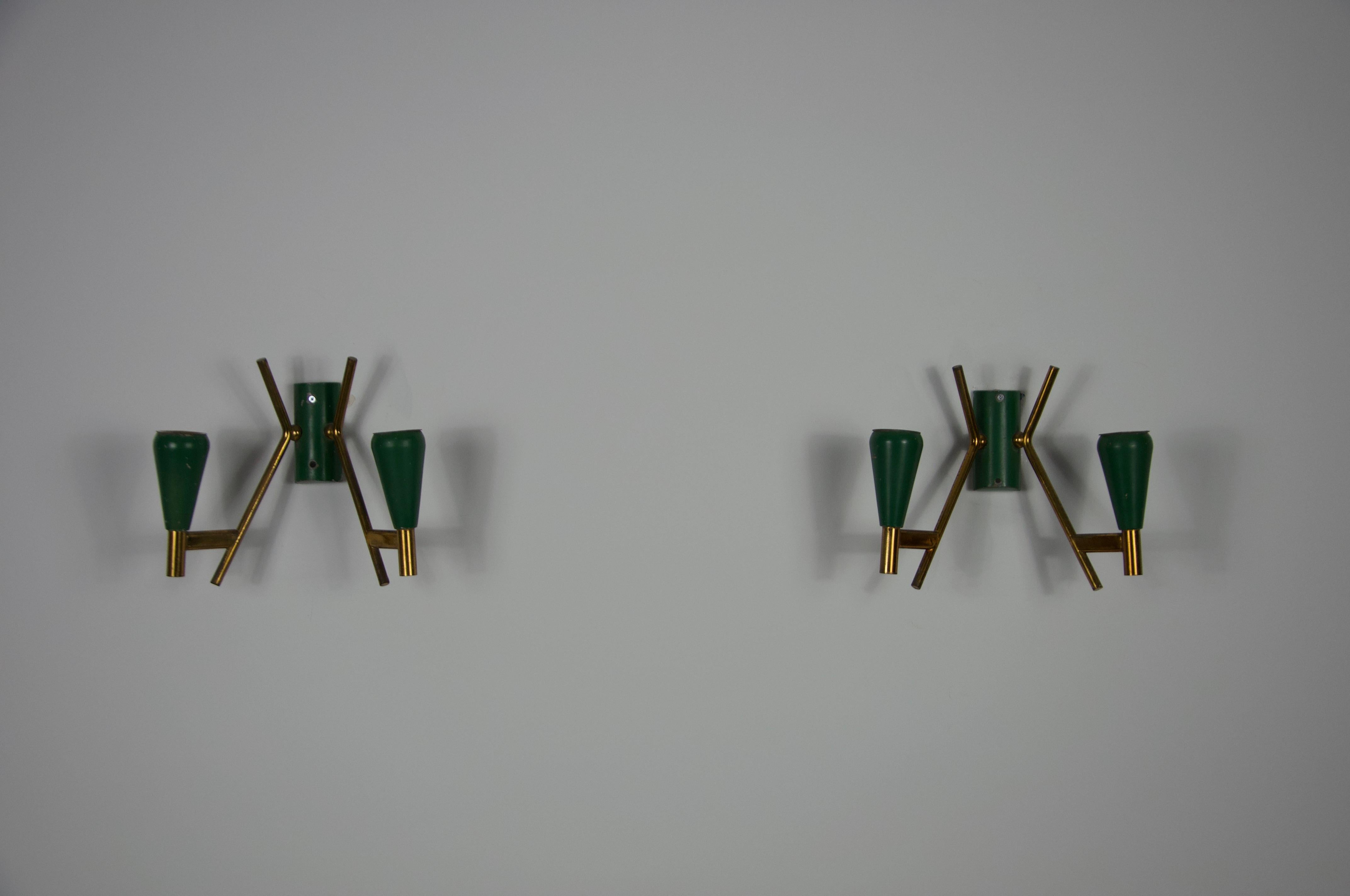 This elegant pair of wall lamps from the 1960s showcases timeless Italian craftsmanship and sophisticated mid-century design. Made of high-quality brass, they feature green bases that create a refined contrast. Each lamp has two gracefully arms,