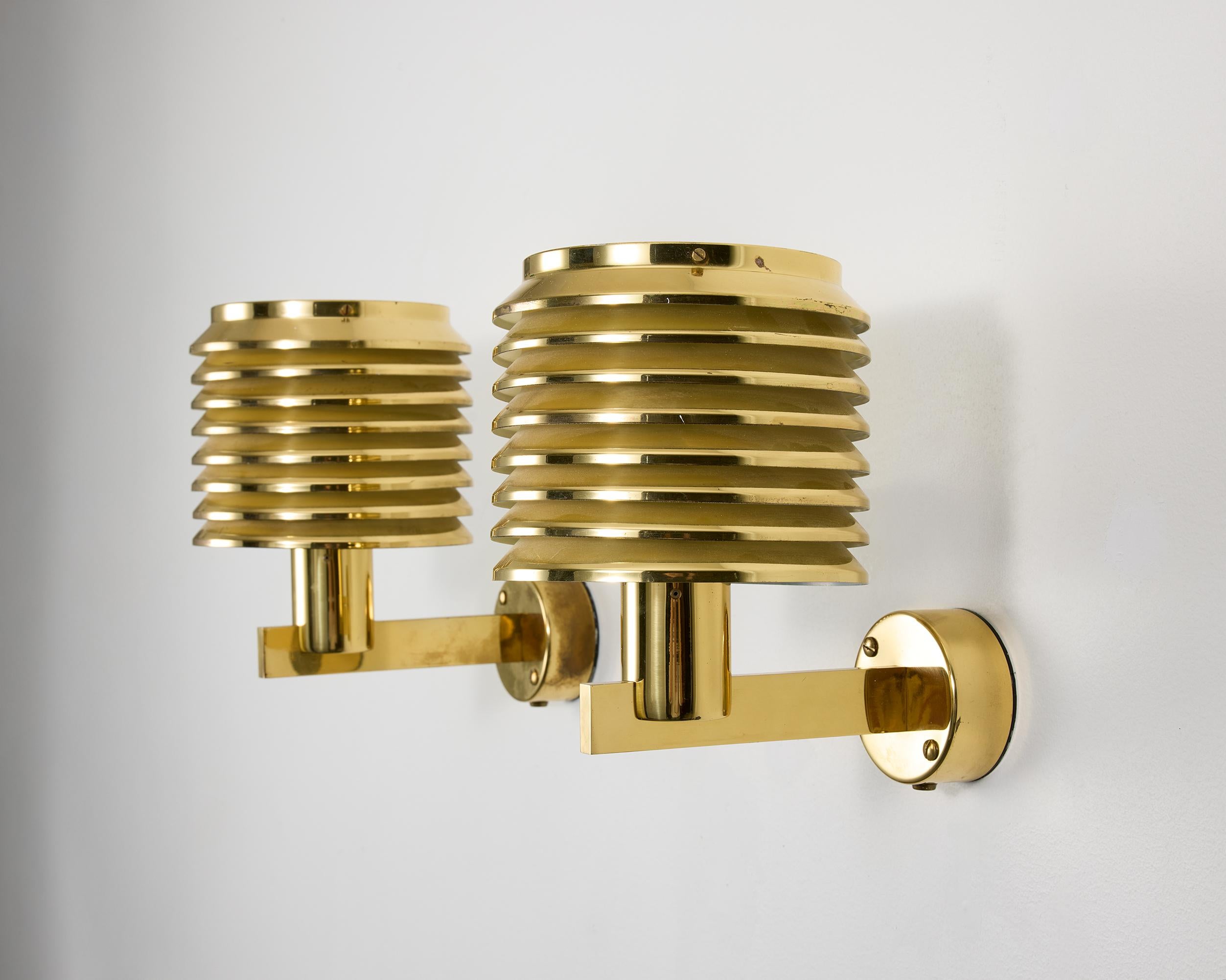 La lámpara de pared modelo V-299 es un gran ejemplo del diseño de iluminación sueco de mediados de siglo, creado por Hans-Agne Jakobsso. Fabricada en latón pulido, la lámpara presenta una pantalla cilíndrica compuesta por anillos concéntricos