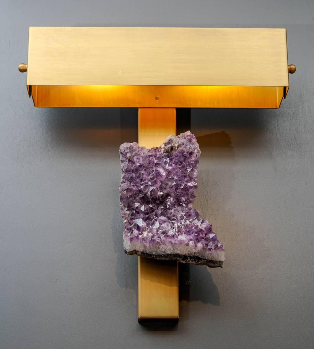Pair of wall sconces made of a long brass backplate, supporting a large amethyst stone under a rectangular shade.