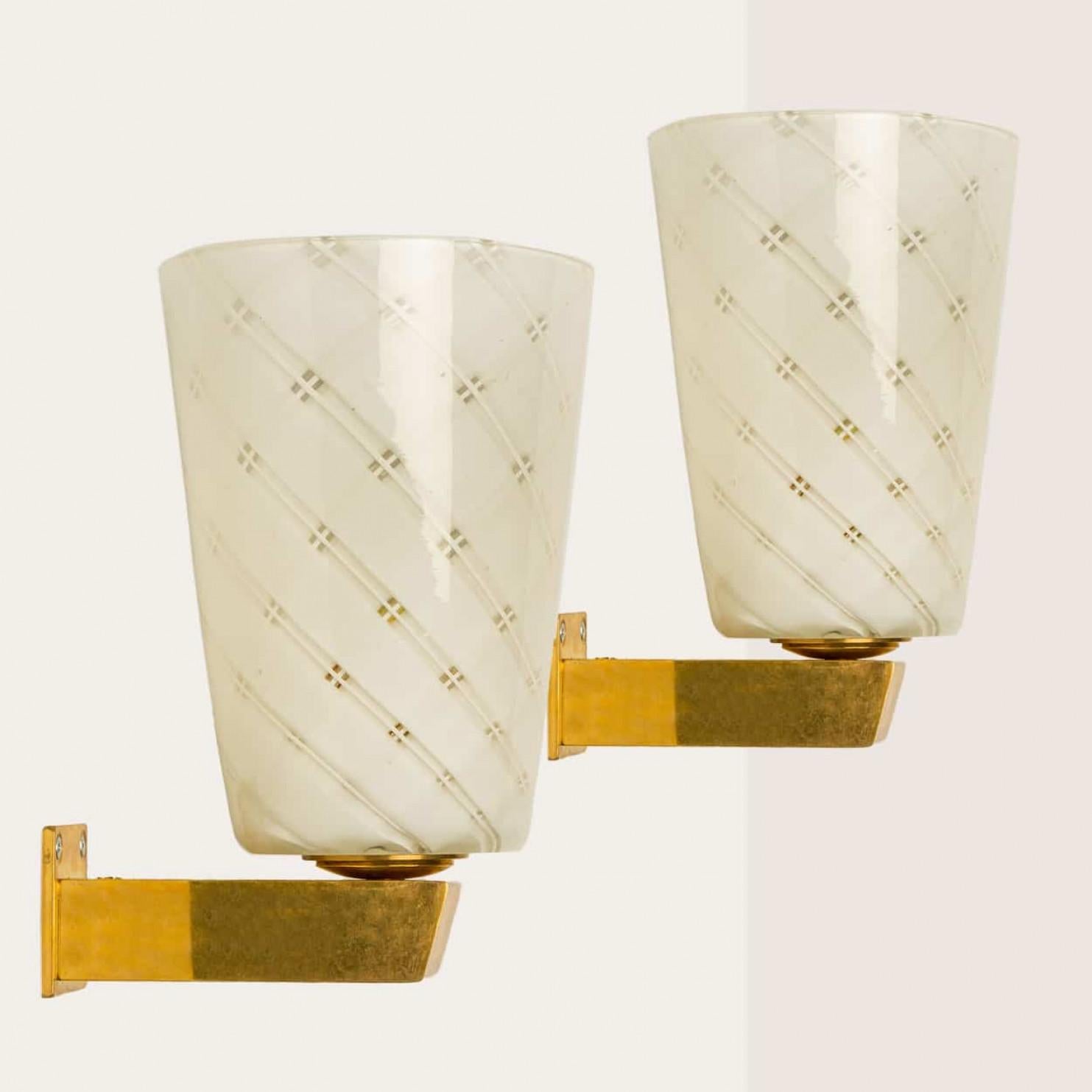 Una delle due bellissime applique in vetro reticello soffiato a mano con base in ottone, nello stile di Seguso, circa anni '50 - '60.

Il vetro reticello diffonde la luce in un motivo ipnotico, riflettendo linee incrociate sulla parete.

Il